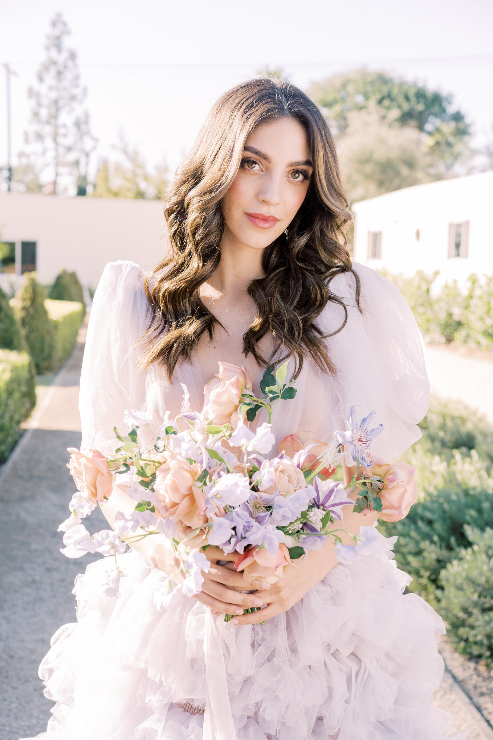 Portrait of a bride in a lavender wedding gown in a garden holding a bouquet.