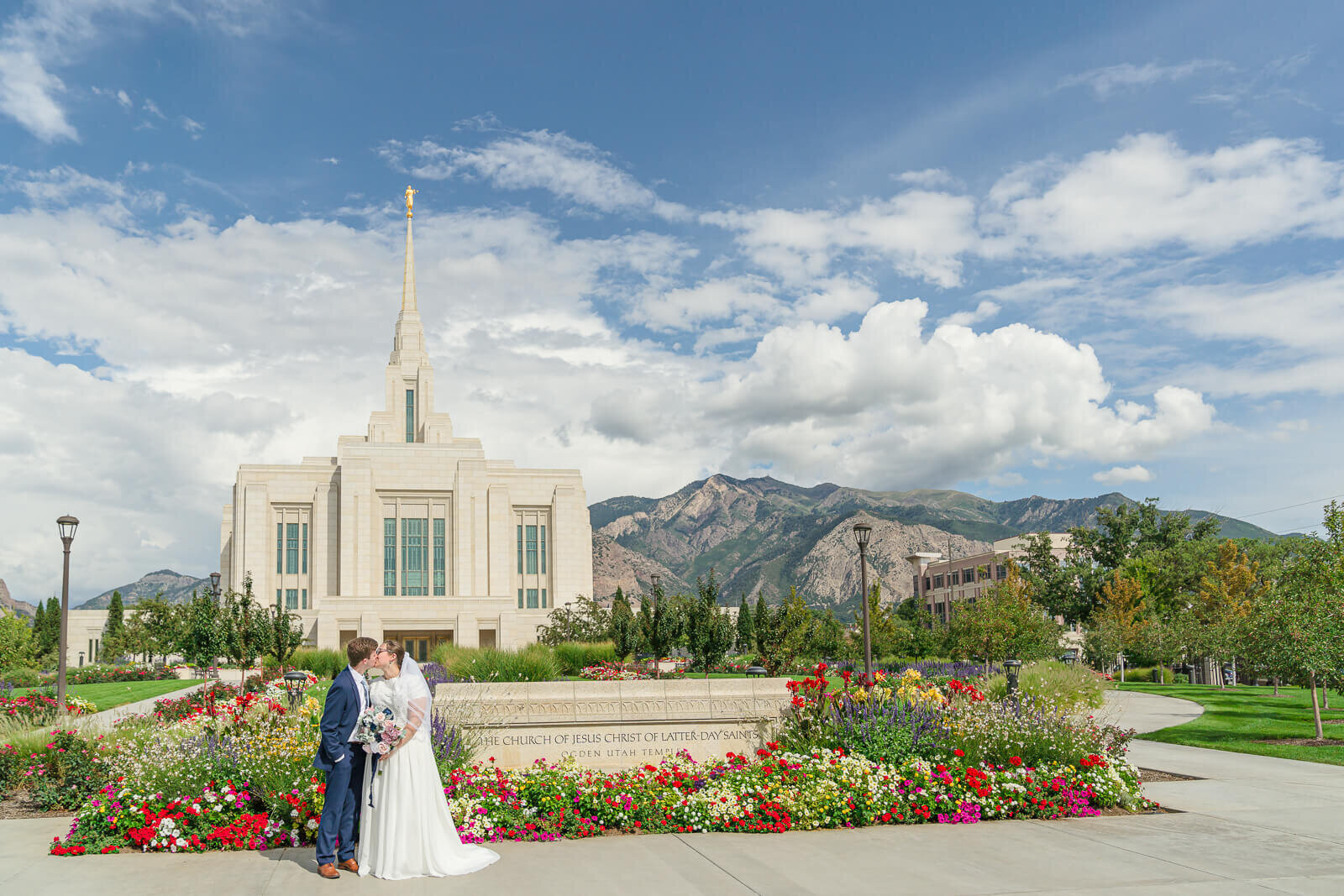 bride and groom kiss in front of flower beds with a full view of the ogden temple in the background. Captured by Salt Lake Photographer Melissa Woodruff Photography