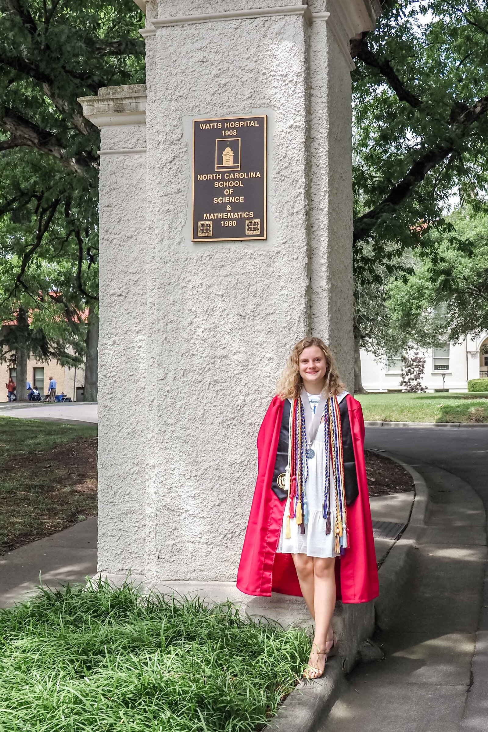 A North Carolina School of Science and Math senior in a red graduation gown standing by a historical monument in Durham, North Carolina. This elegant photo celebrates academic achievement, perfect for those seeking professional and memorable senior photography.
