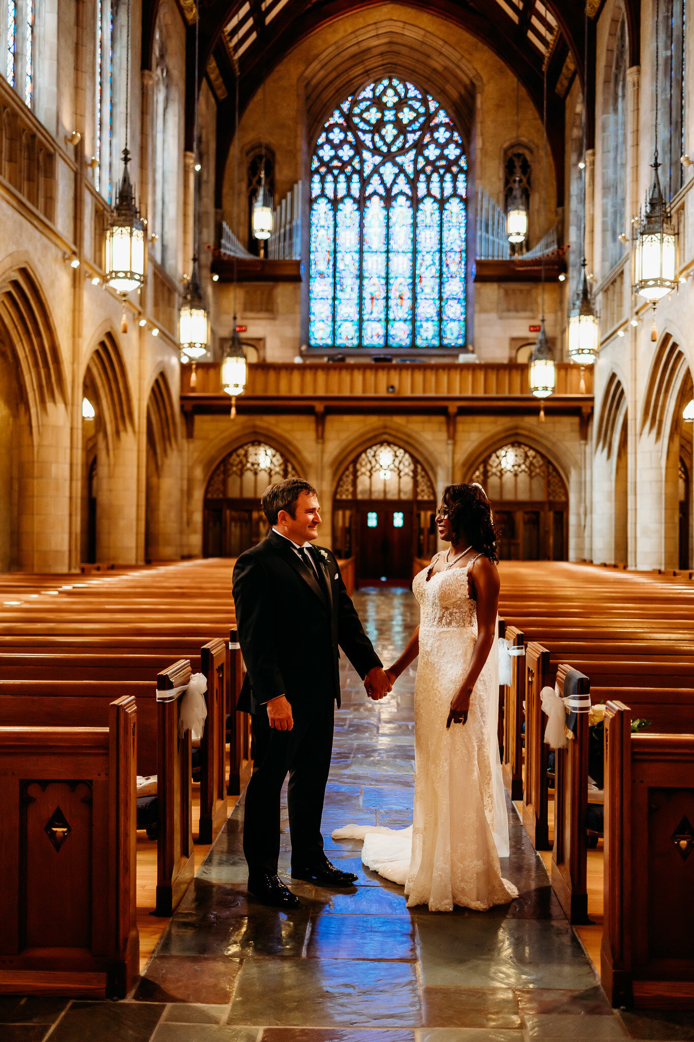 A bride and groom stand hand in hand in the isle of a gorgeous cathedral church in Erie PA