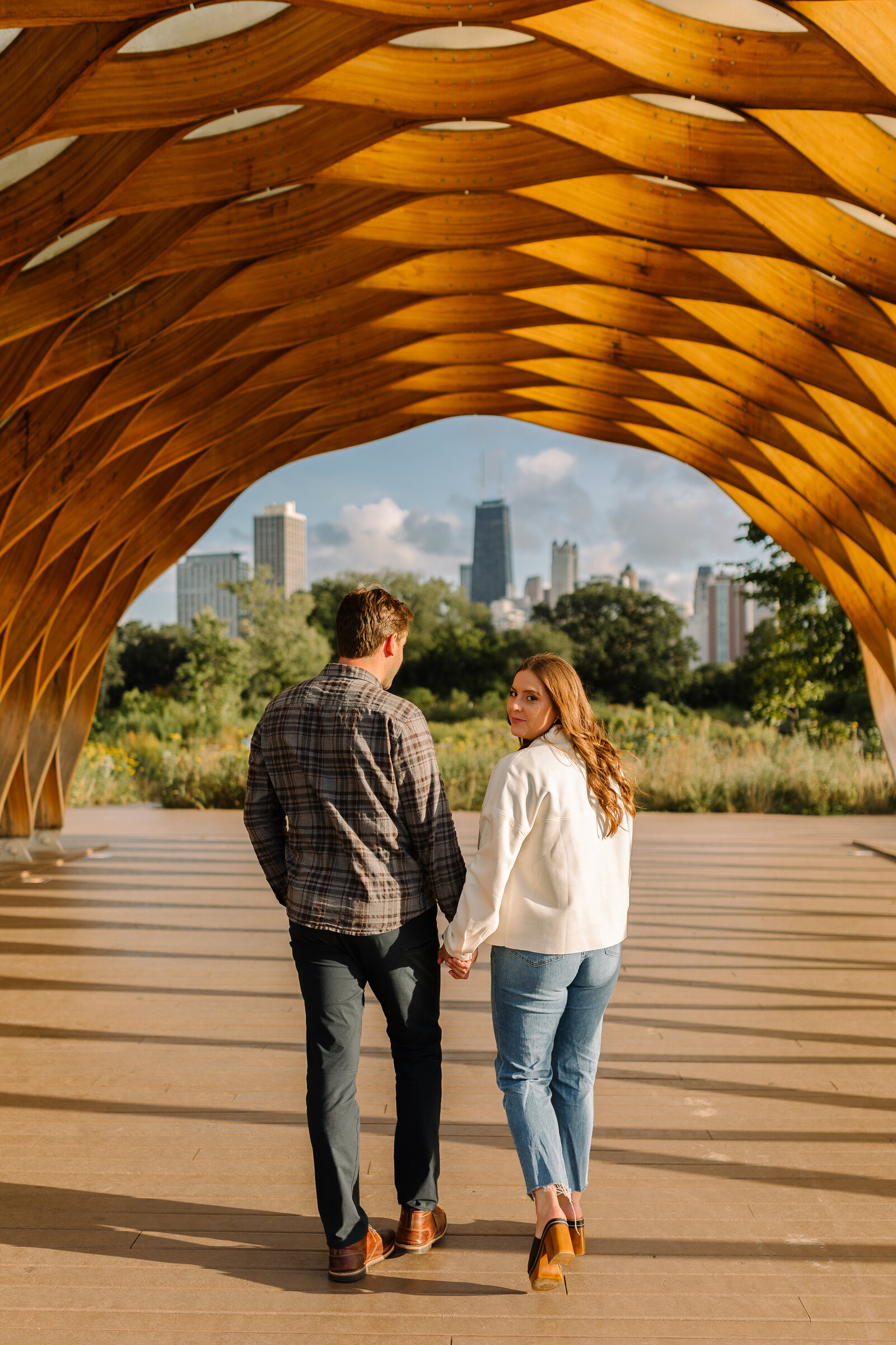 Newly engaged couple walking together while hugging each other under the honeycomb sculpture in Chicago