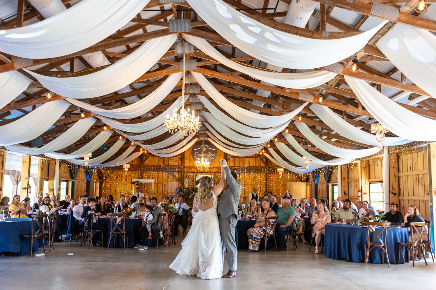 Bride and groom dancing under draped fabric and chandeliers with guests seated around