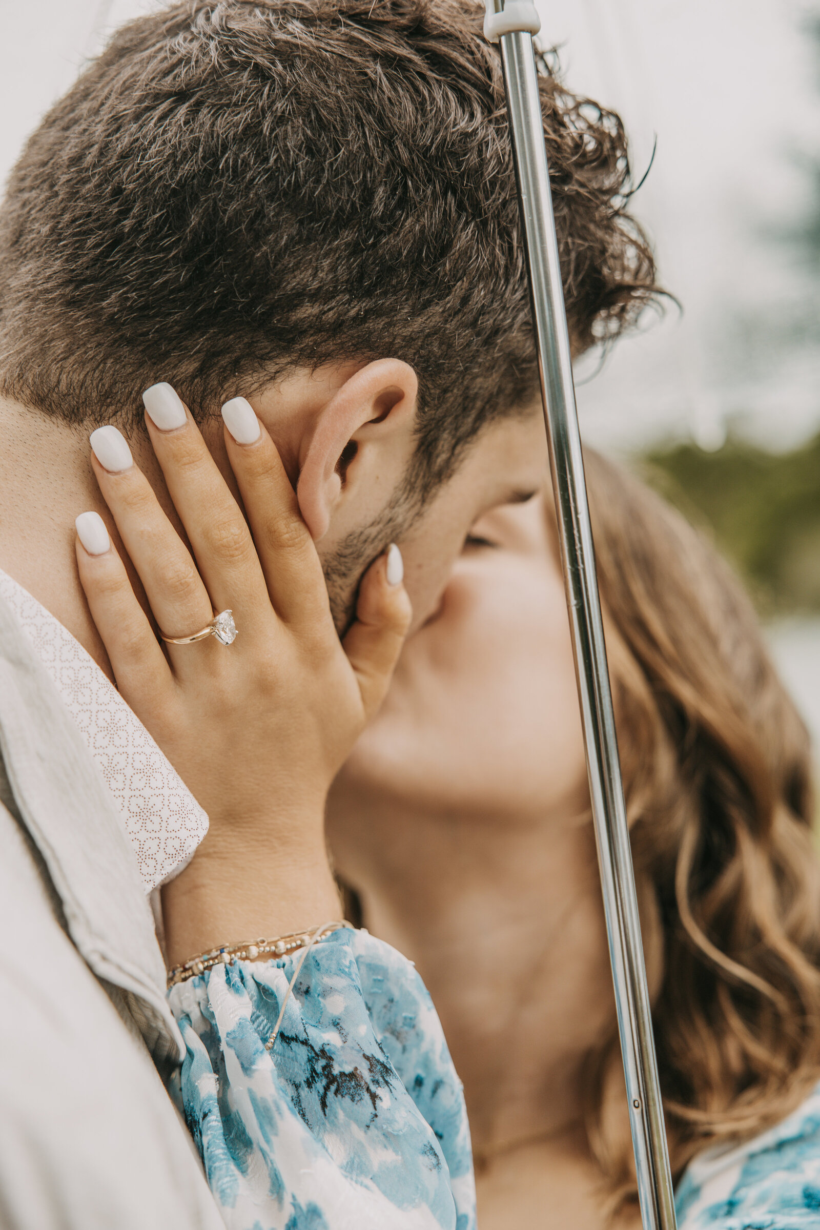 Man and woman share a kiss during their engagement session on a rainy day at Shelby Farms Park, with focus on the woman's engagement ring.