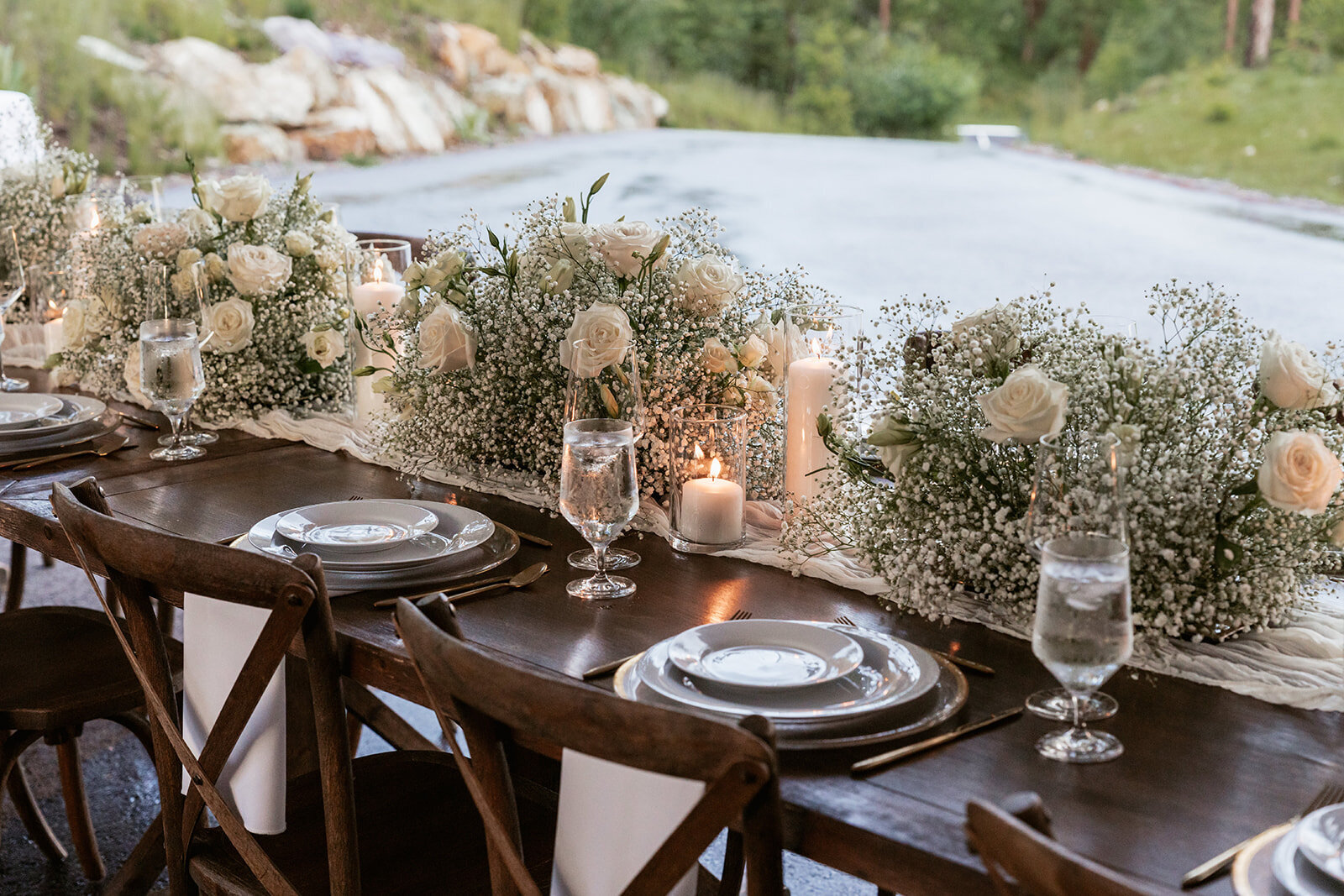 Romantic table design for an intimate elopement dinner featuring baby’s breath, white roses, and glowing candles with mountain views in the background.