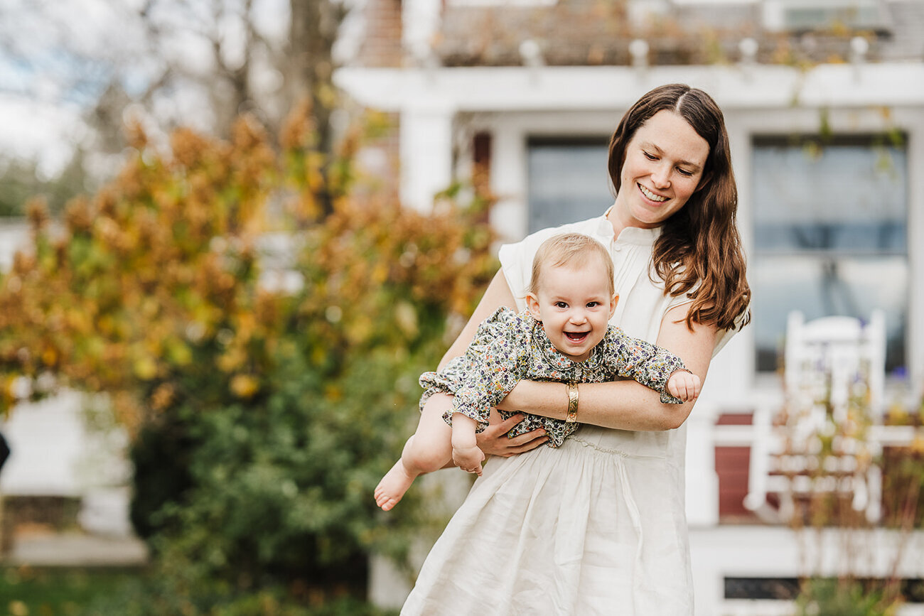 baby girl laughs as mother flies her through the air in backyard boston photo session