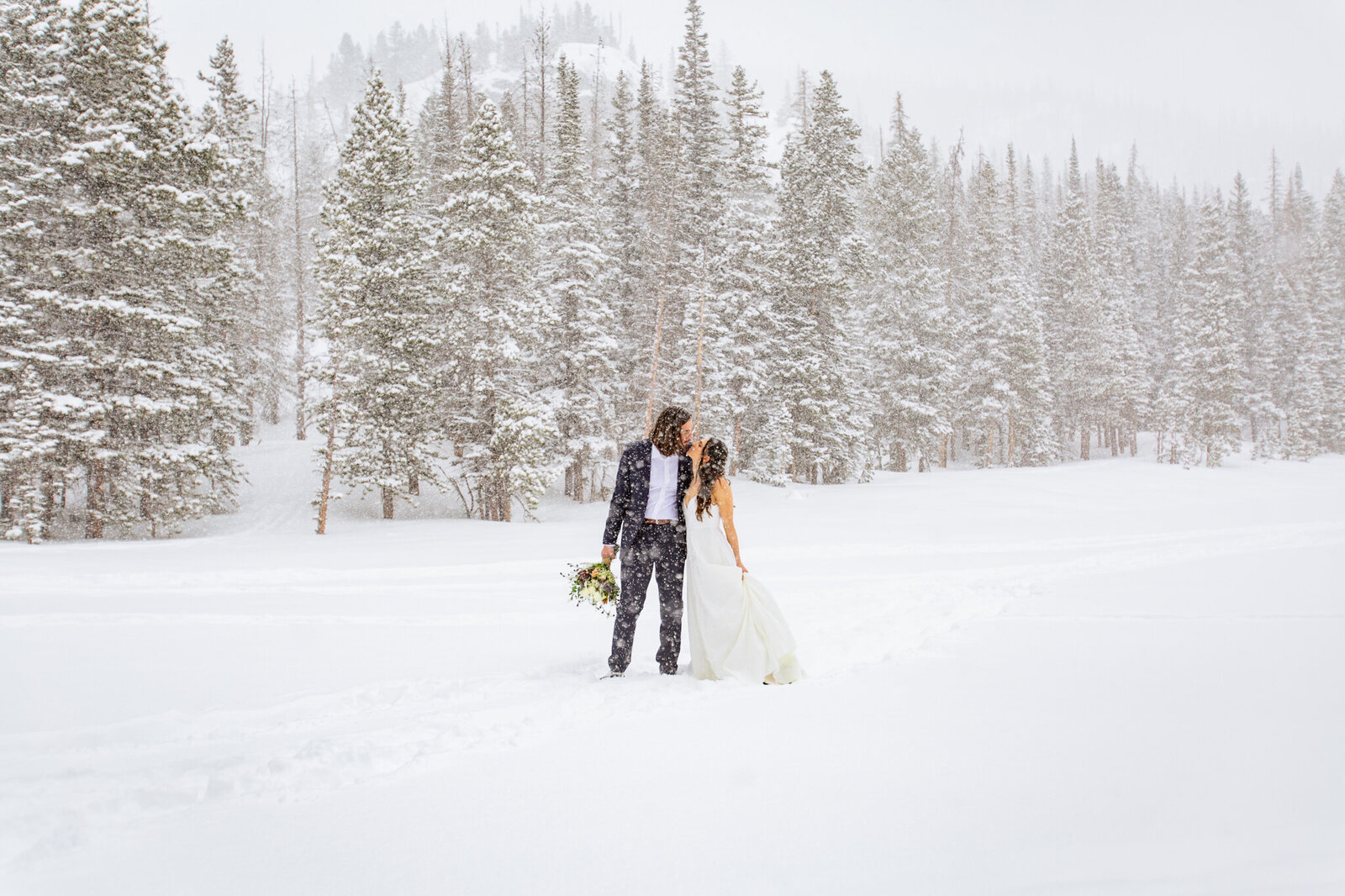 Bride and groom kiss on a frozen lake during a snow storm in rocky mountain national park