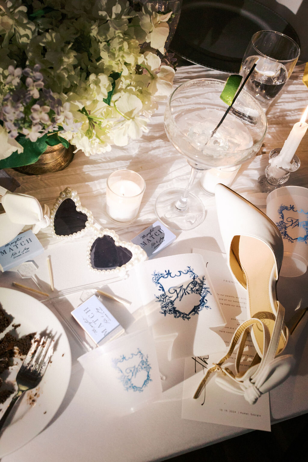 White bridal shoes, heart glasses, and wedding invitations with martini glass on reception tables