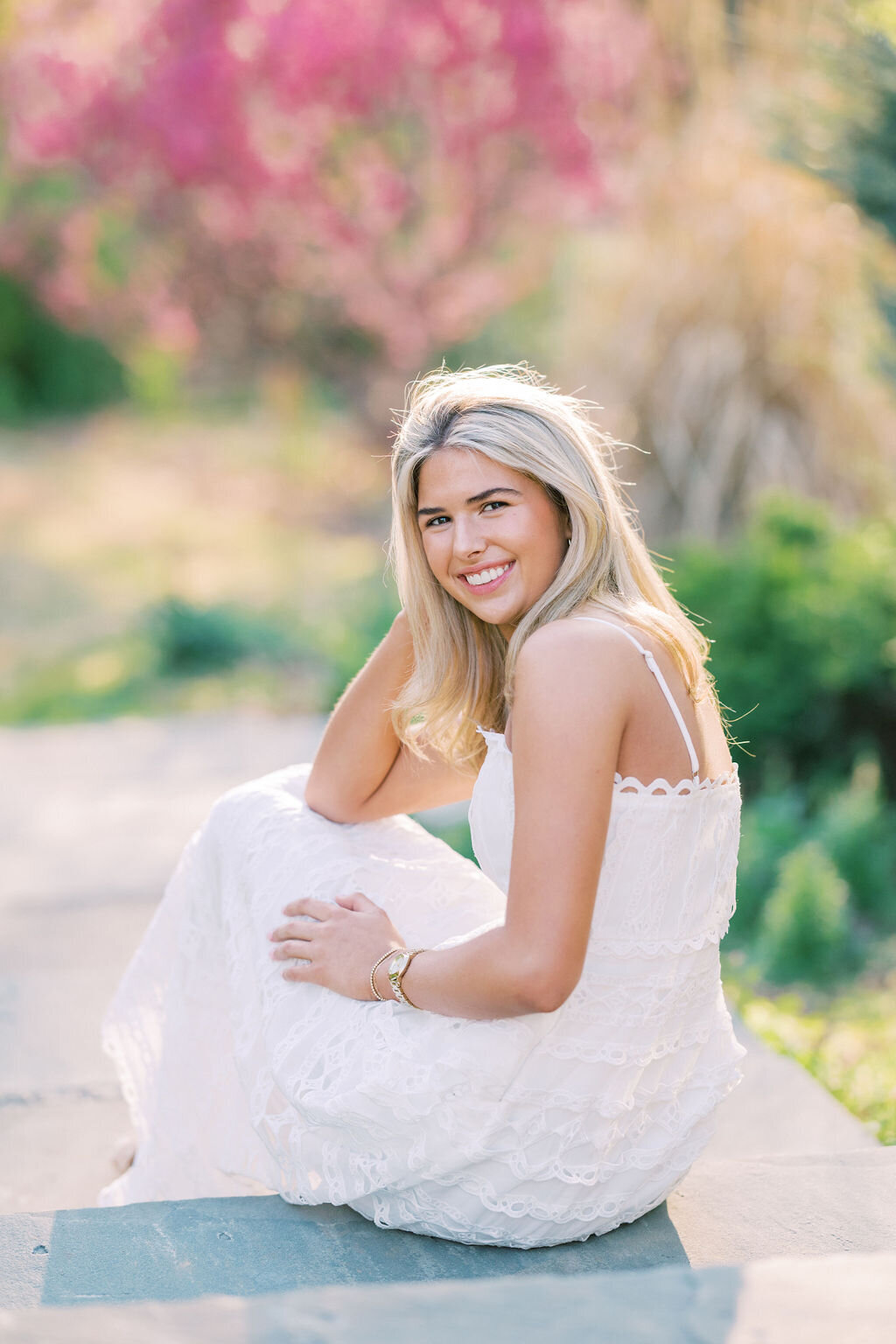 Senior girl in white dress tucks hair behind ear at Athens Botanical gardens