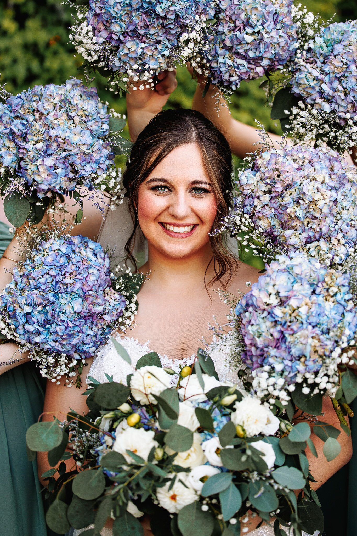A gorgeous brunette bride with a styled updo surrounded by a frame of her bridesmaids floral bouquets 