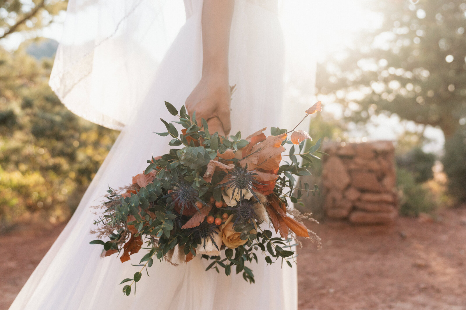 Close-up of bride holding a fall-inspired bouquet with orange leaves, berries, and eucalyptus during a Sedona elopement at Merry-Go-Round Rock.