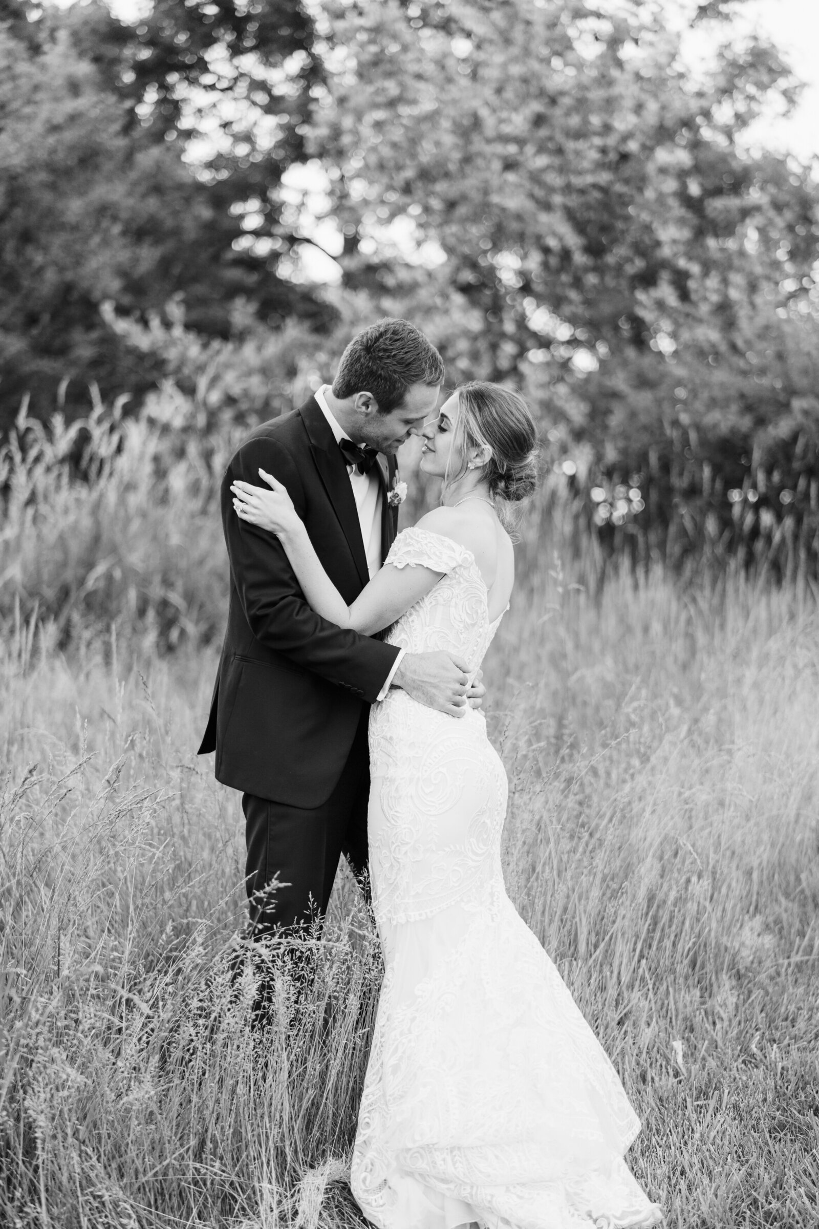 Bride and groom stand in tall grass and share a kiss during blue hour