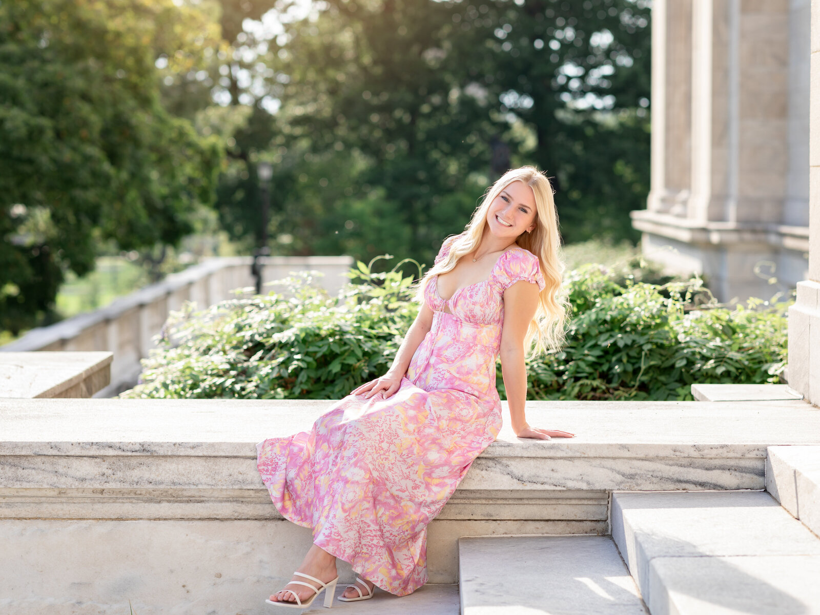 high school senior girl in pink floral dress sitting on marble for senior portraits in cleveland