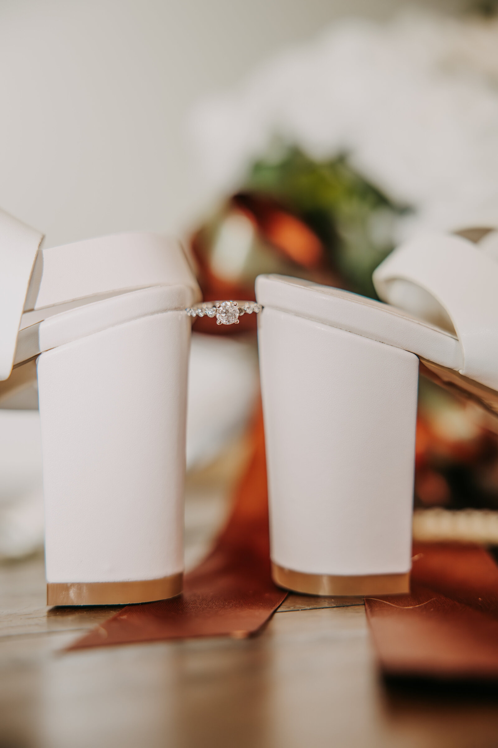 Bride's engagement ring balanced between the heels of her shoes, creating a delicate and elegant bridal detail.