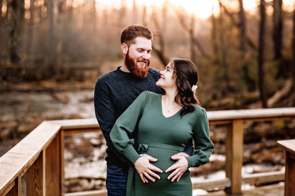 Man holds pregnant  wife's belly from behind as they gaze back at each other