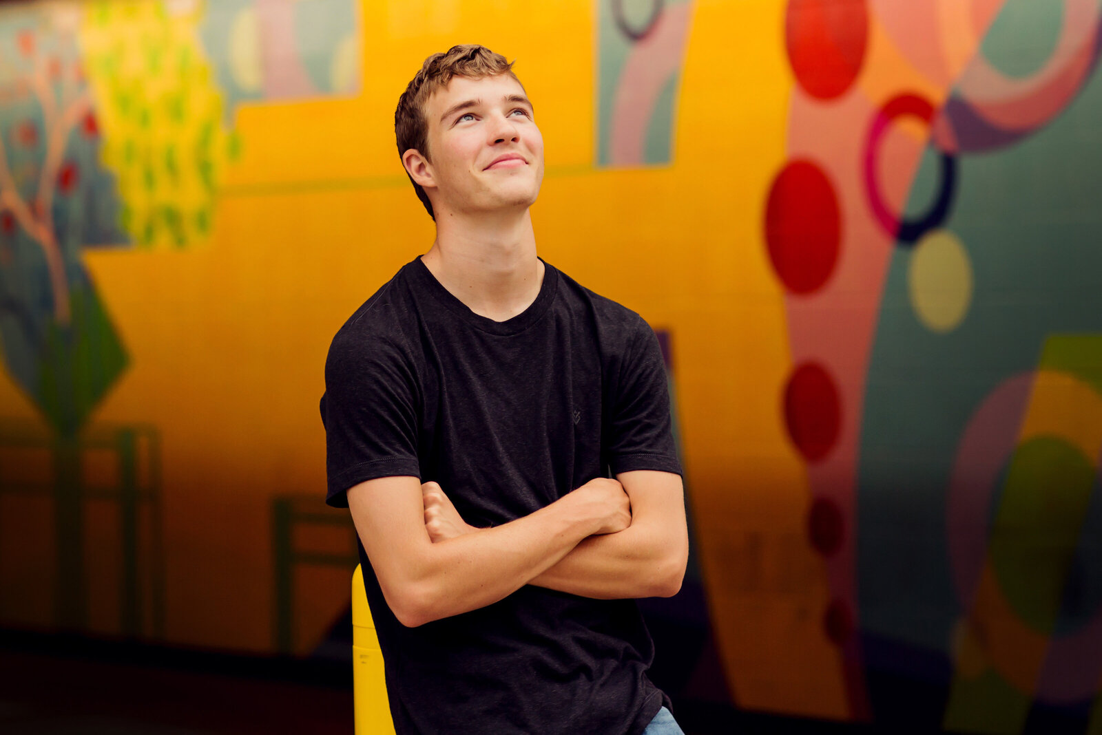 Senior boy looking up towards the sky with a very colorful and geometrical wall behind him.
