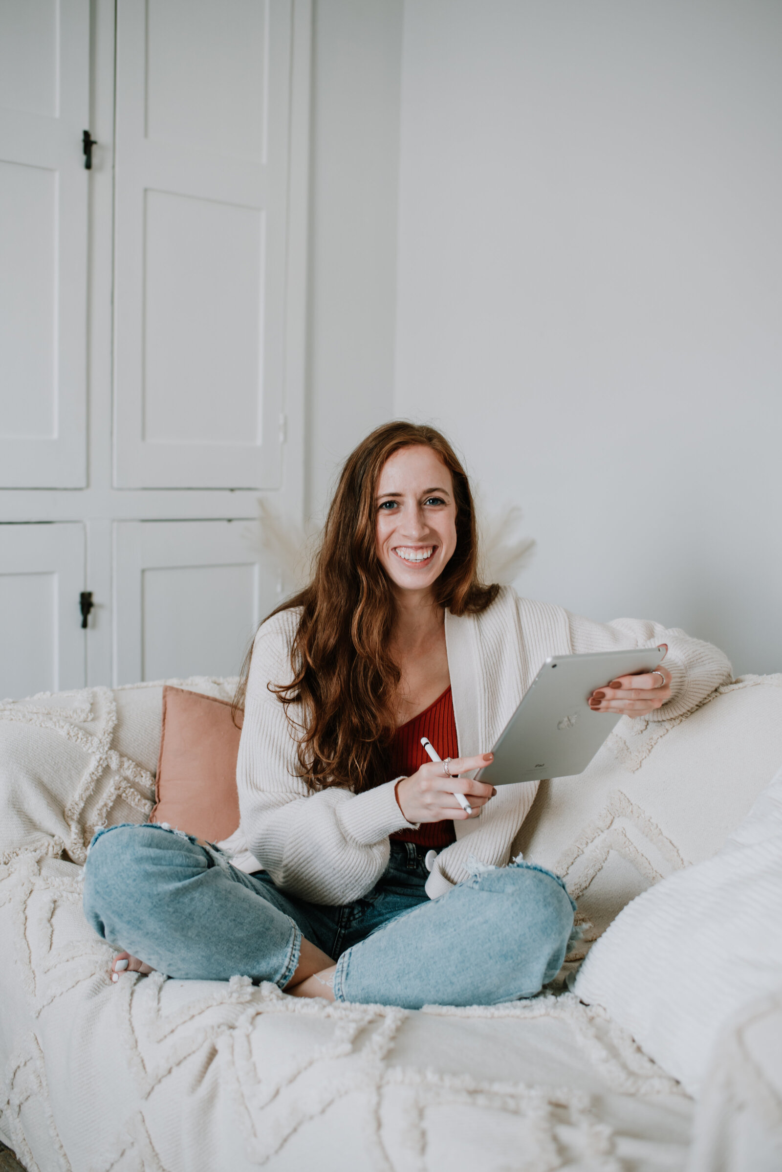 woman dressed in neutral clothing is sat on the sofa, holding a tablet and e-pen, smiling