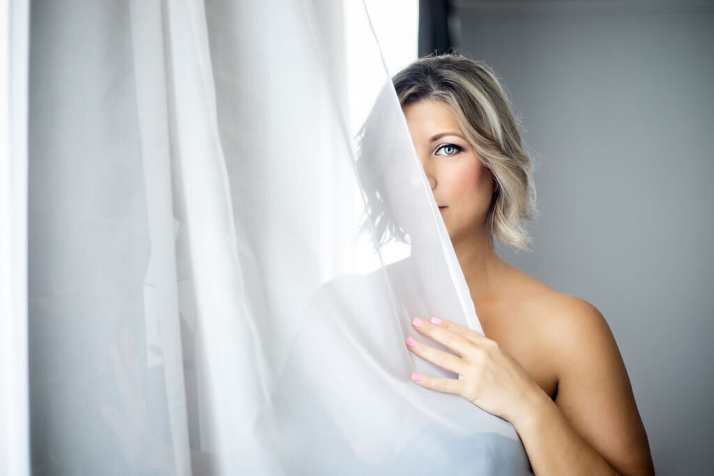 portrait of woman hiding behind sheer white curtain