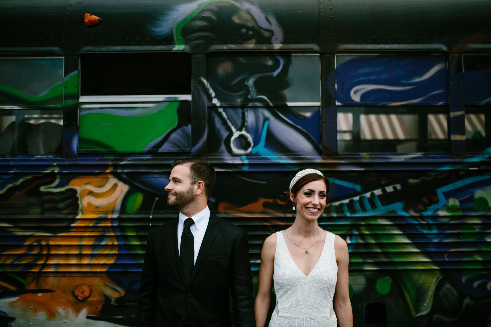 Bride and groom pose for portrait in front of bus covered in graffiti