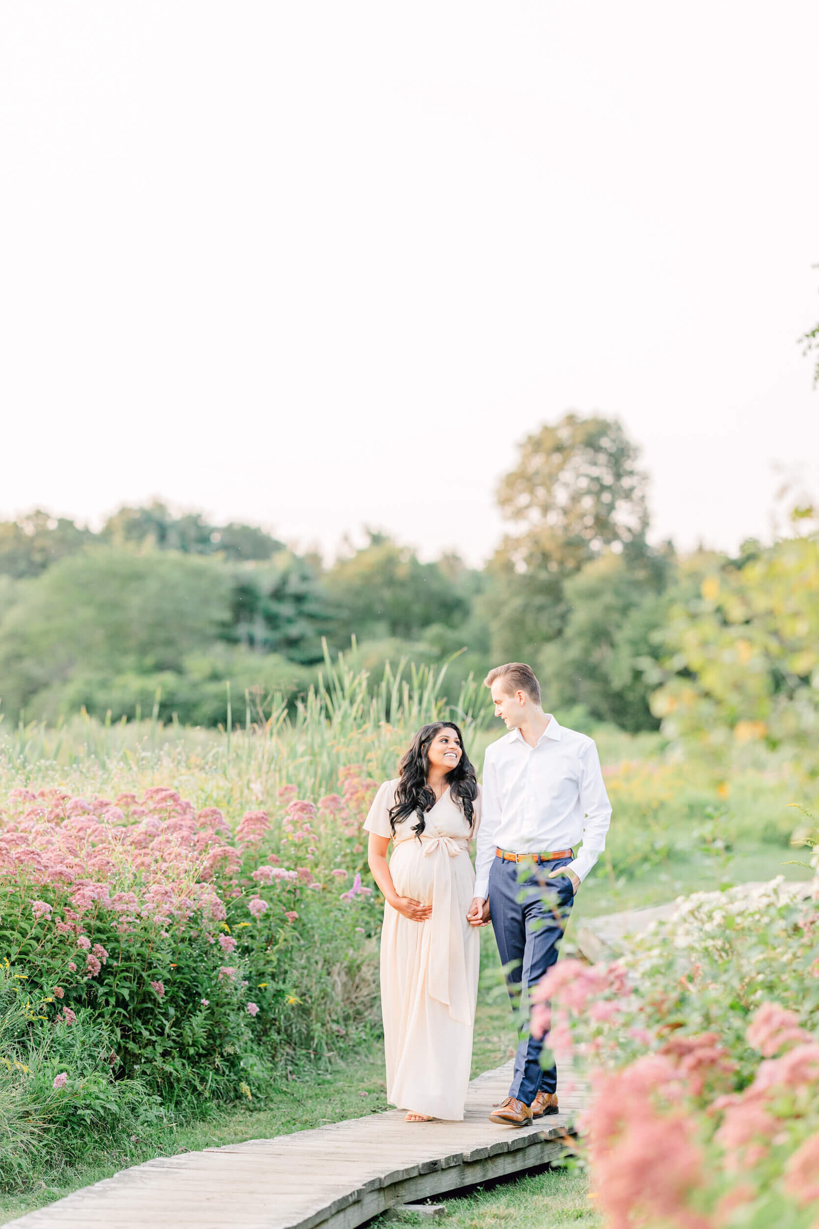 Pregnant woman and husband hold hands and smile at each other while they