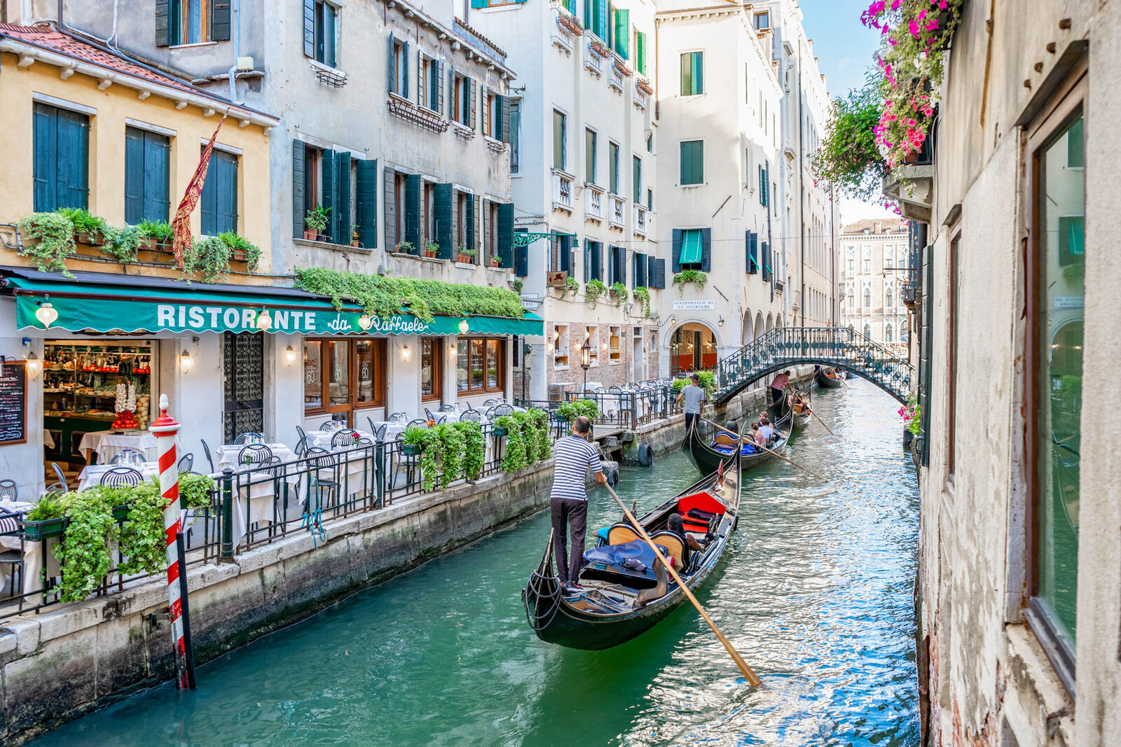 A beautiful view of a Venice canal with gondolas and gondoliers passing by canal front restaurants.
