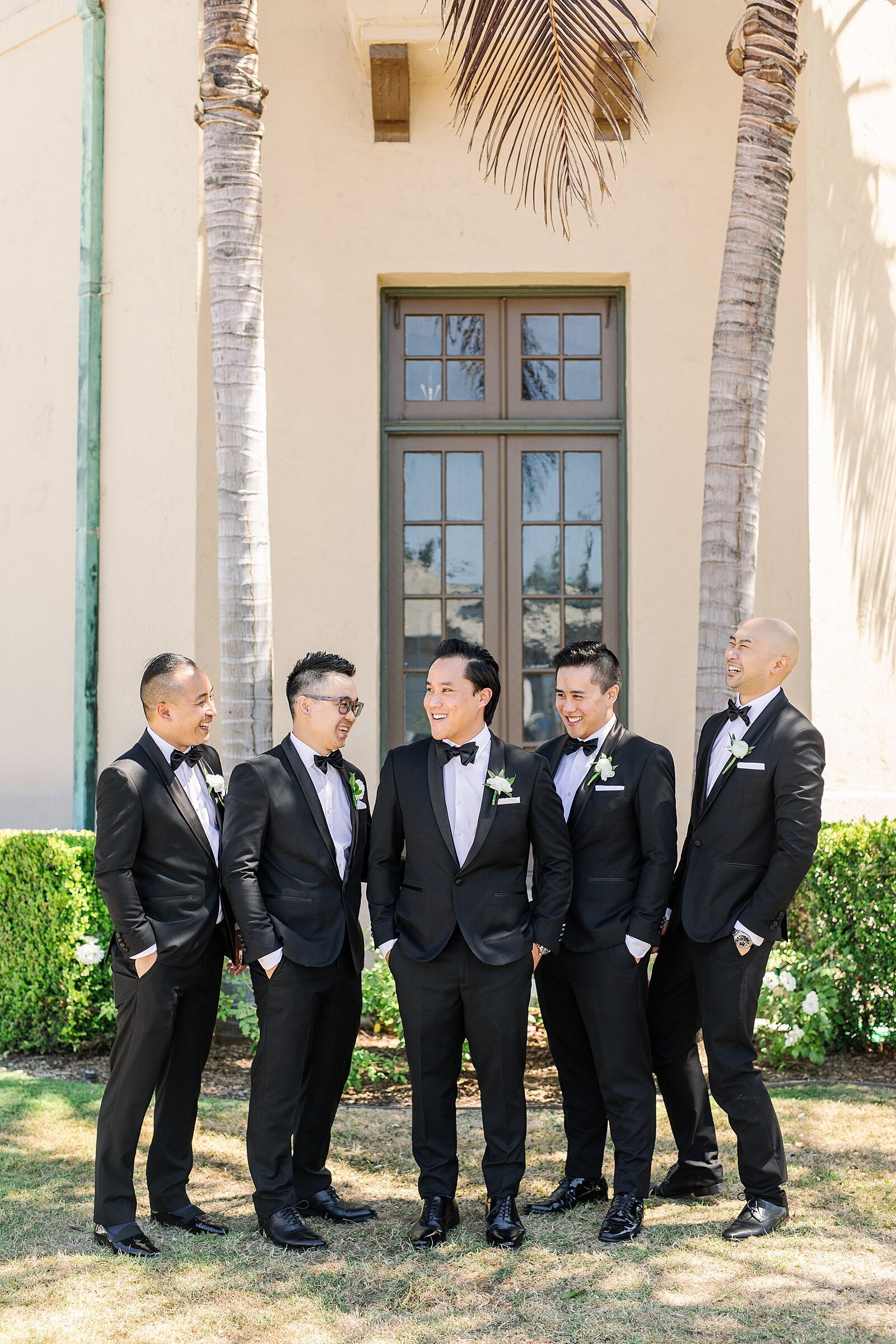 Groom and groomsmen laughing together in tuxes in front of the Fairmount Grand Del Mar in San Diego, California photographed and filmed by Sherr Weddings.