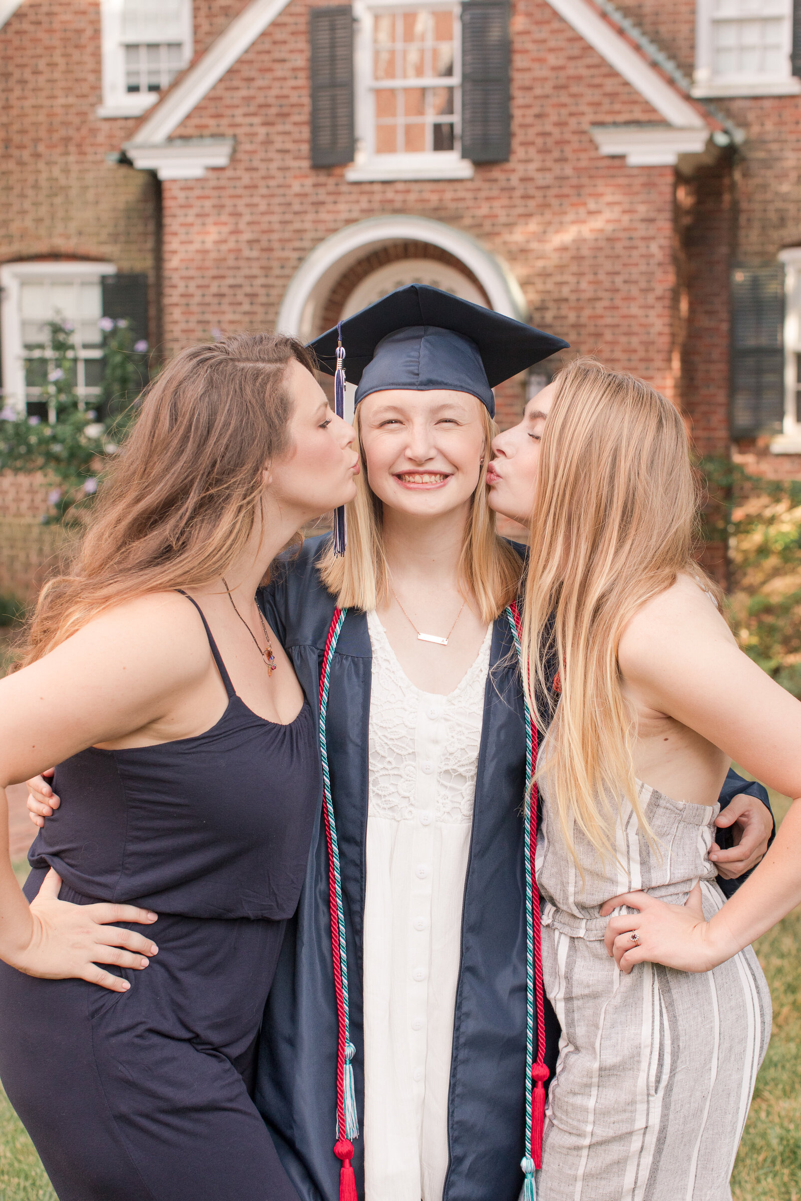senior girl in cap and gown being kissed on cheeks by sisters