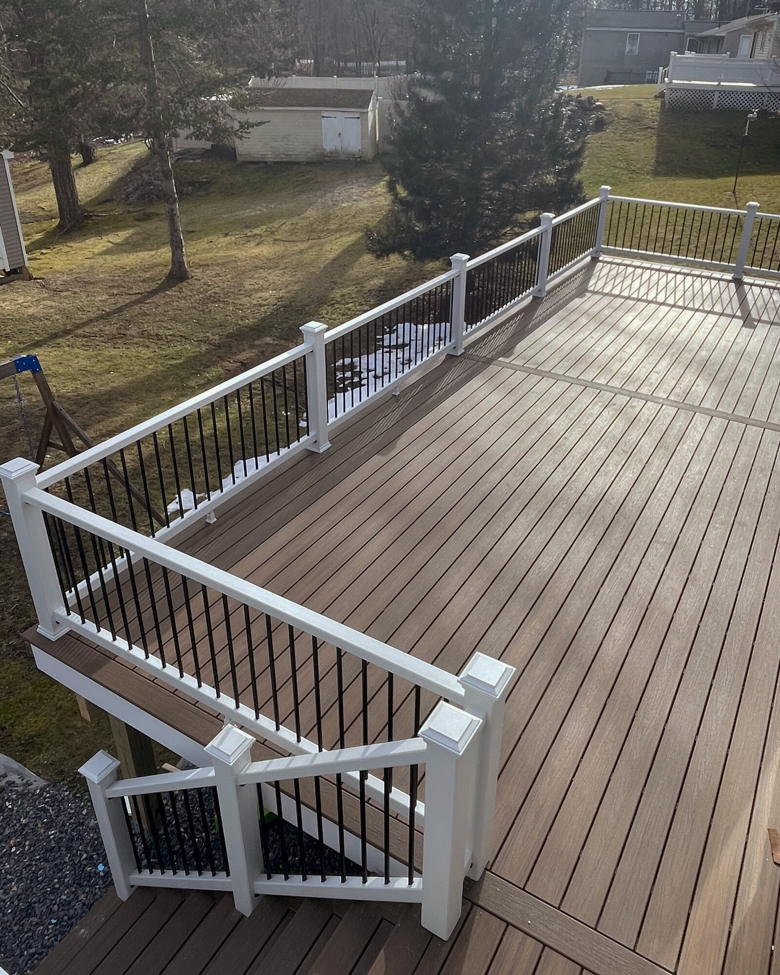 A brown composite deck with white and black railings with steps leading to lawn