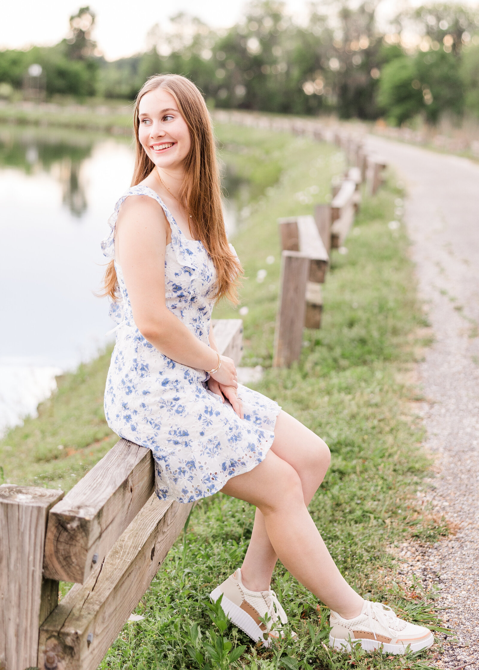Sophie leaning on a wooden fence near a tranquil lake, showcasing her senior portrait by Abby Bell Photography, Fine Art Portrait Photographer based in Alabama.