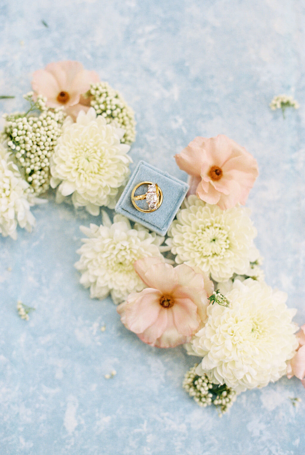 Pink and white flowers on blue flat lay background with wedding rings