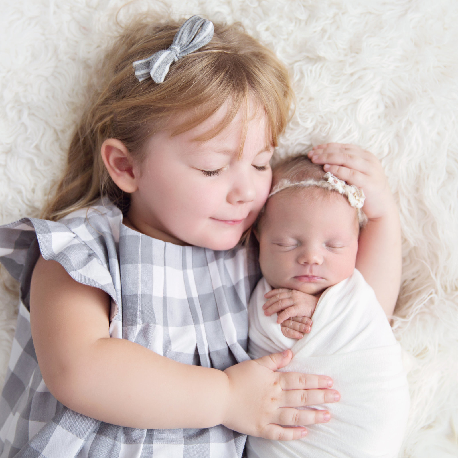 sleeping newborn baby wrapped with big sister sibling eyes closed