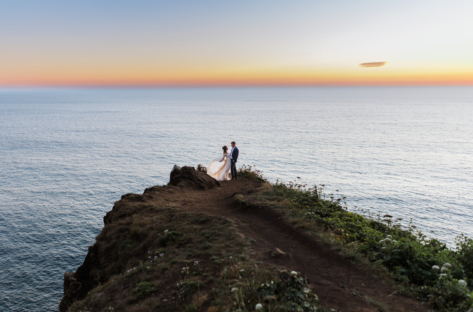 A playful, adventurous couple dancing atop rugged rocks with towering cliffs in the background. This photo showcases the wild, untamed beauty of Oregon's elopement locations.