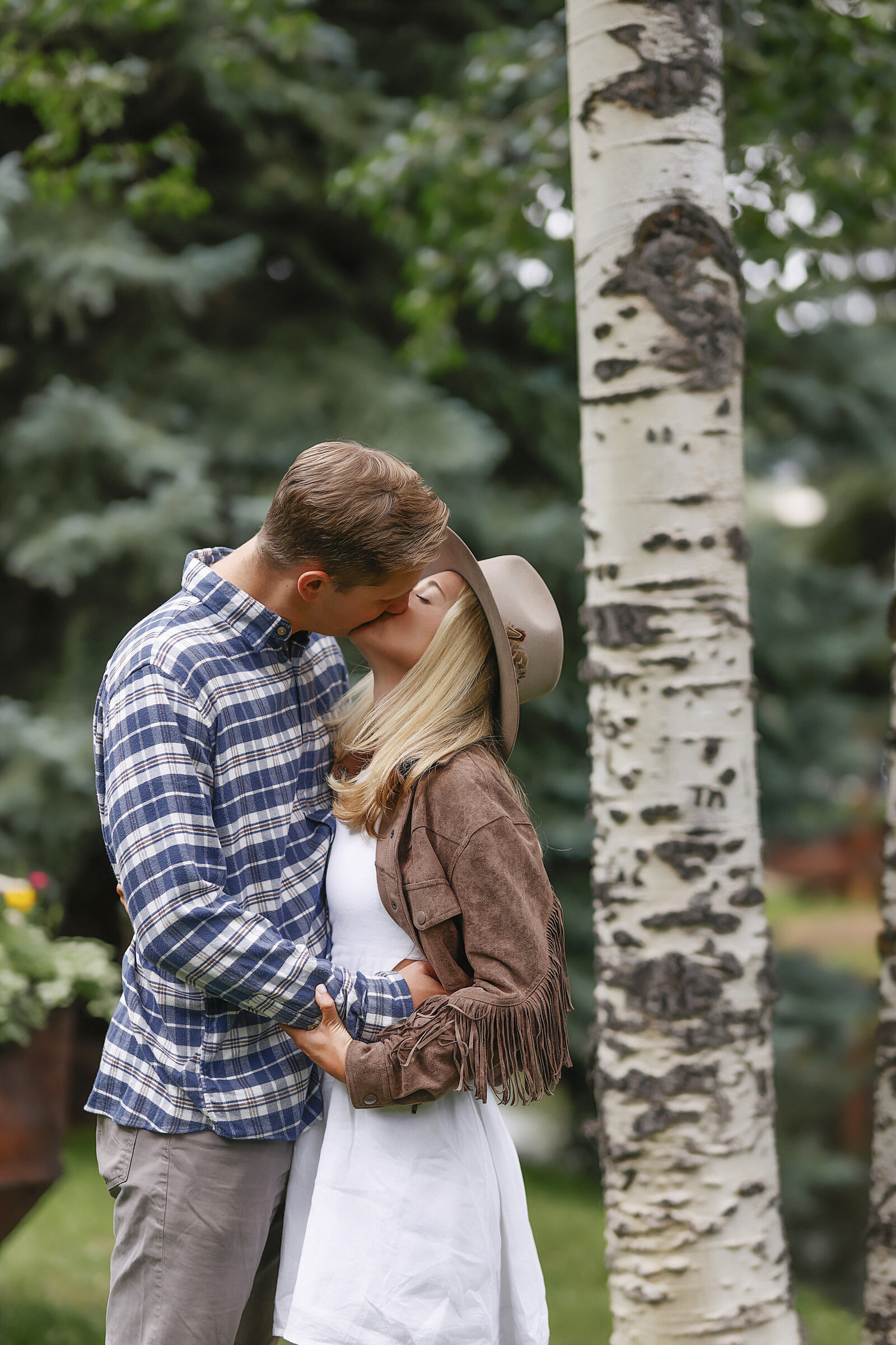 A beautiful couple kiss by an aspen tree in a park in Aspen, Colorado after their surprise mountain top proposal.