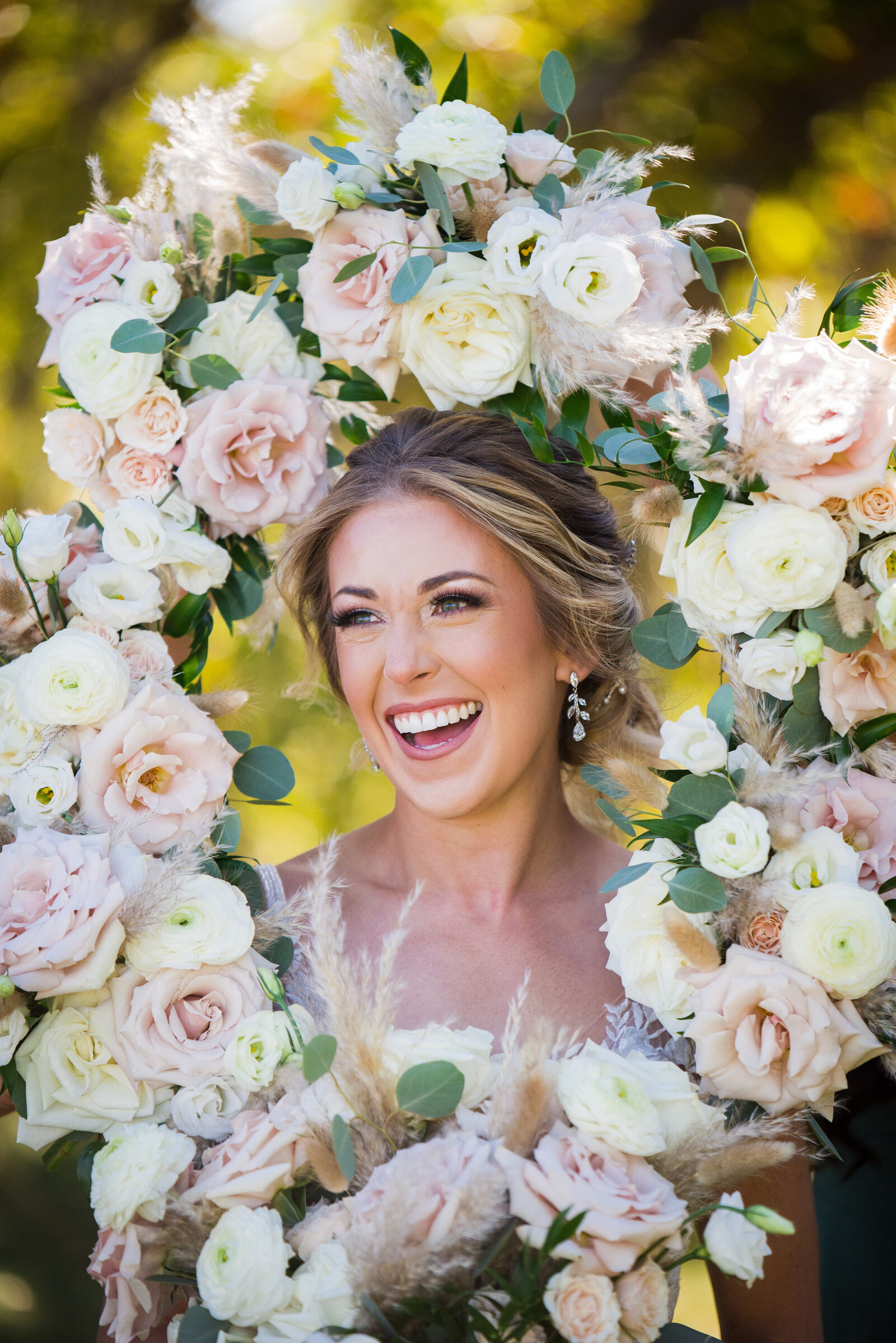 A bride laughs candidly as her bridesmaids frame her faced with their bouquets.