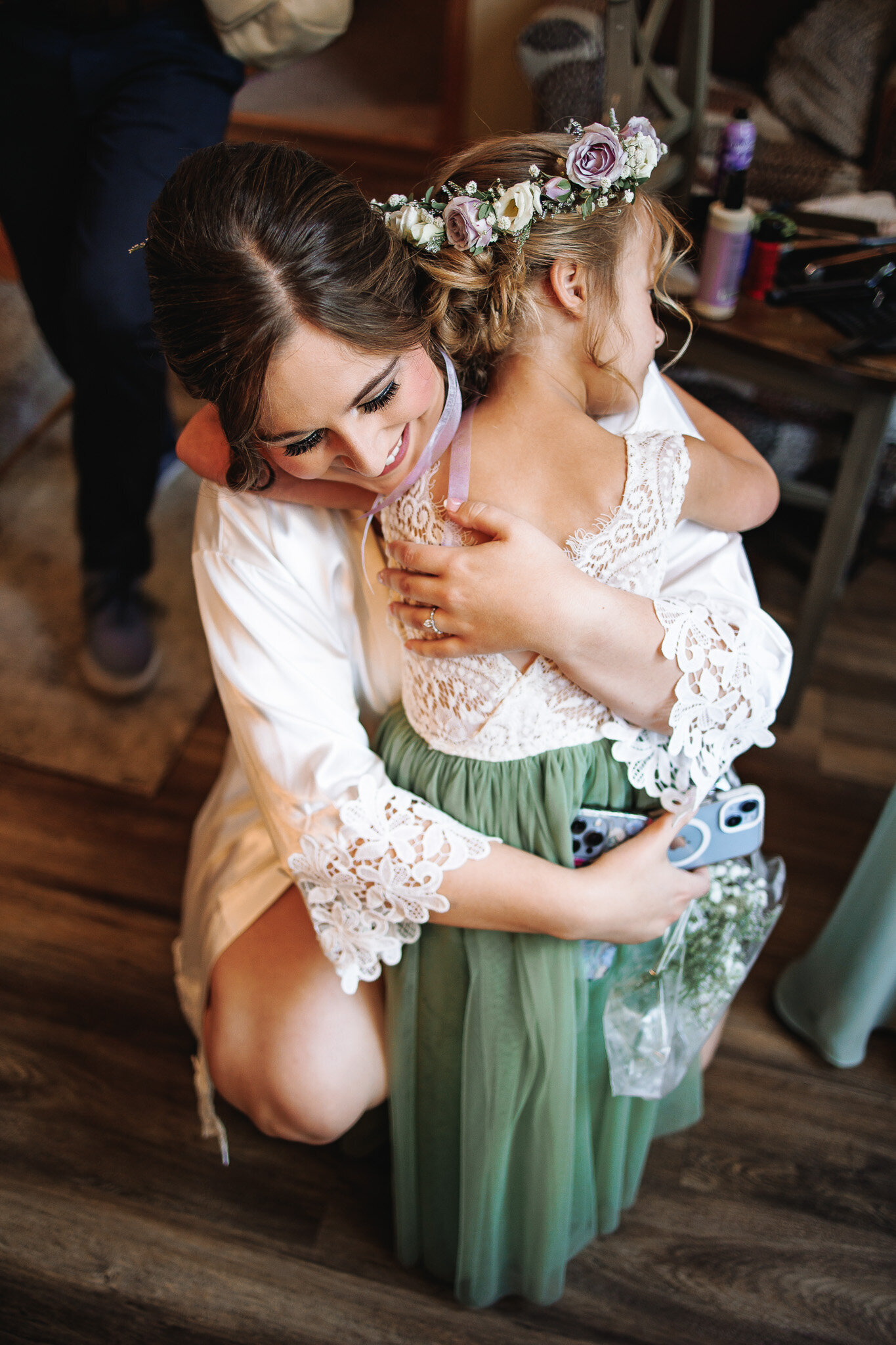 Bride shares a hug with her flower girl in a sage green and white lace dress