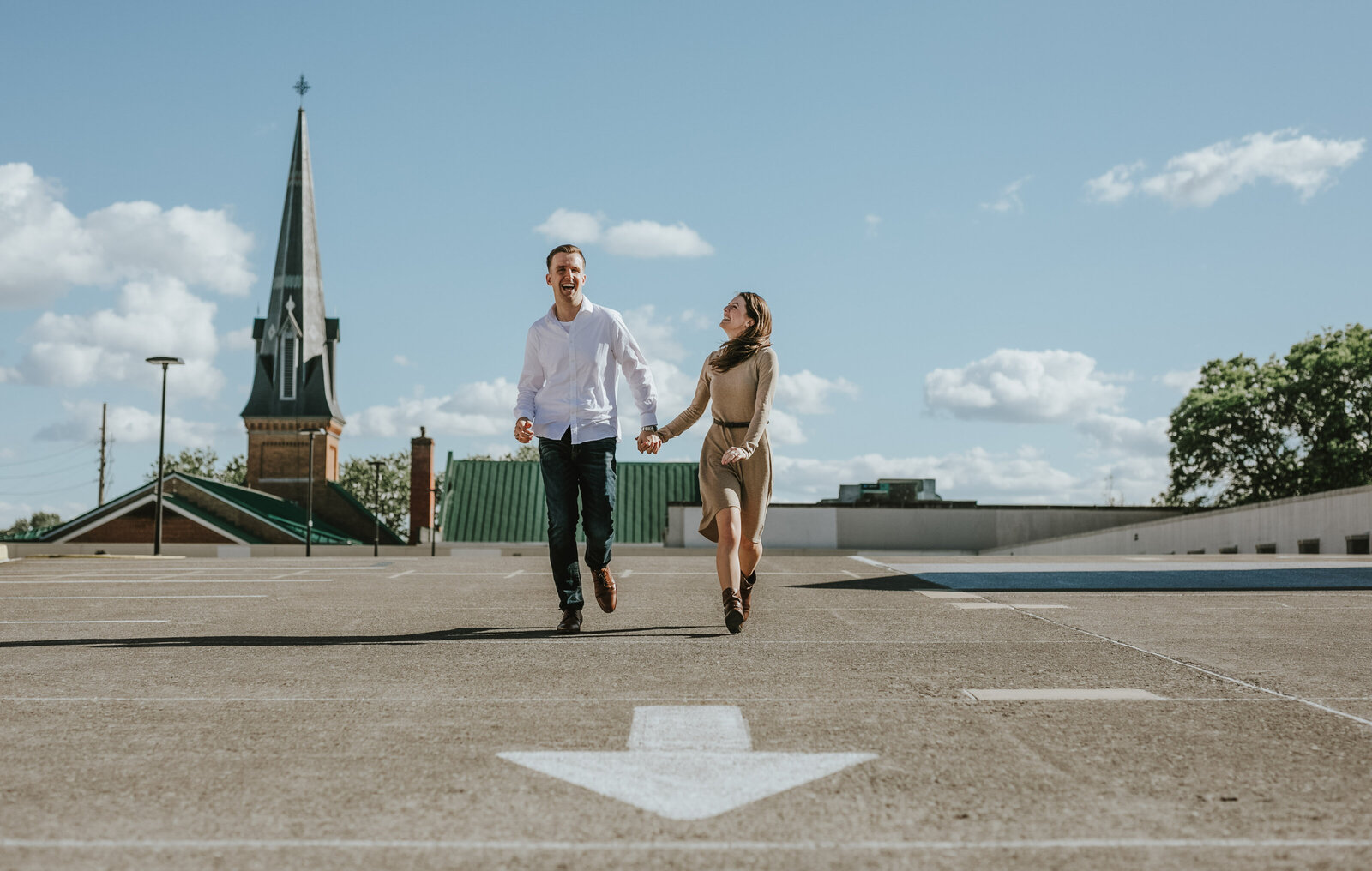 A man and woman hold hands and run on the roof of a parking garage