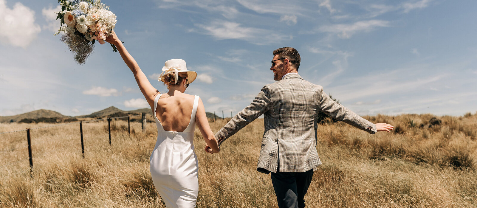 bride groom mountaintop holding hands bouquet hat blenheim wither hills wedding sunny day summer walking away in dry grass