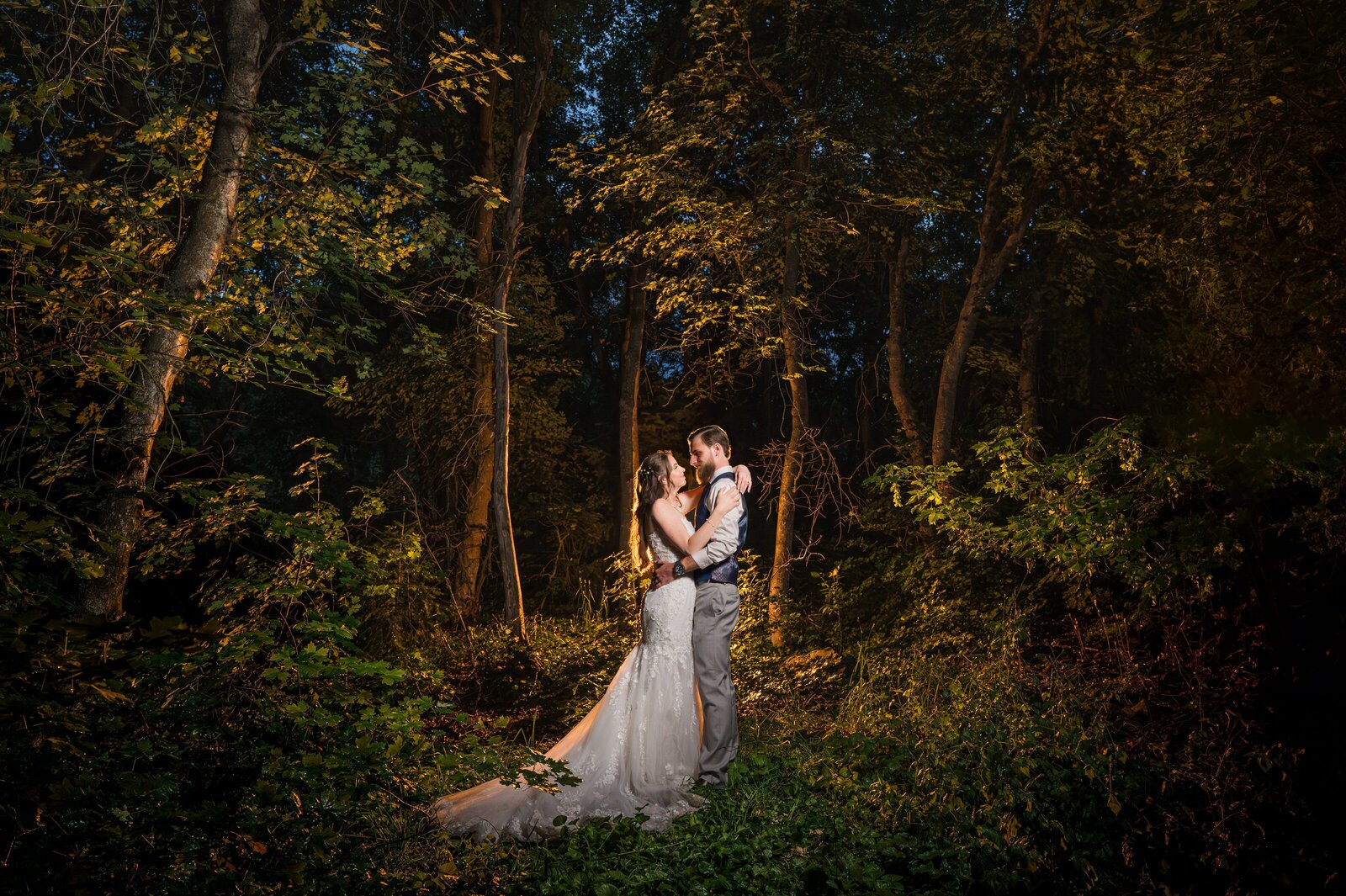 Bride and groom in the forest at night surrounded by trees.