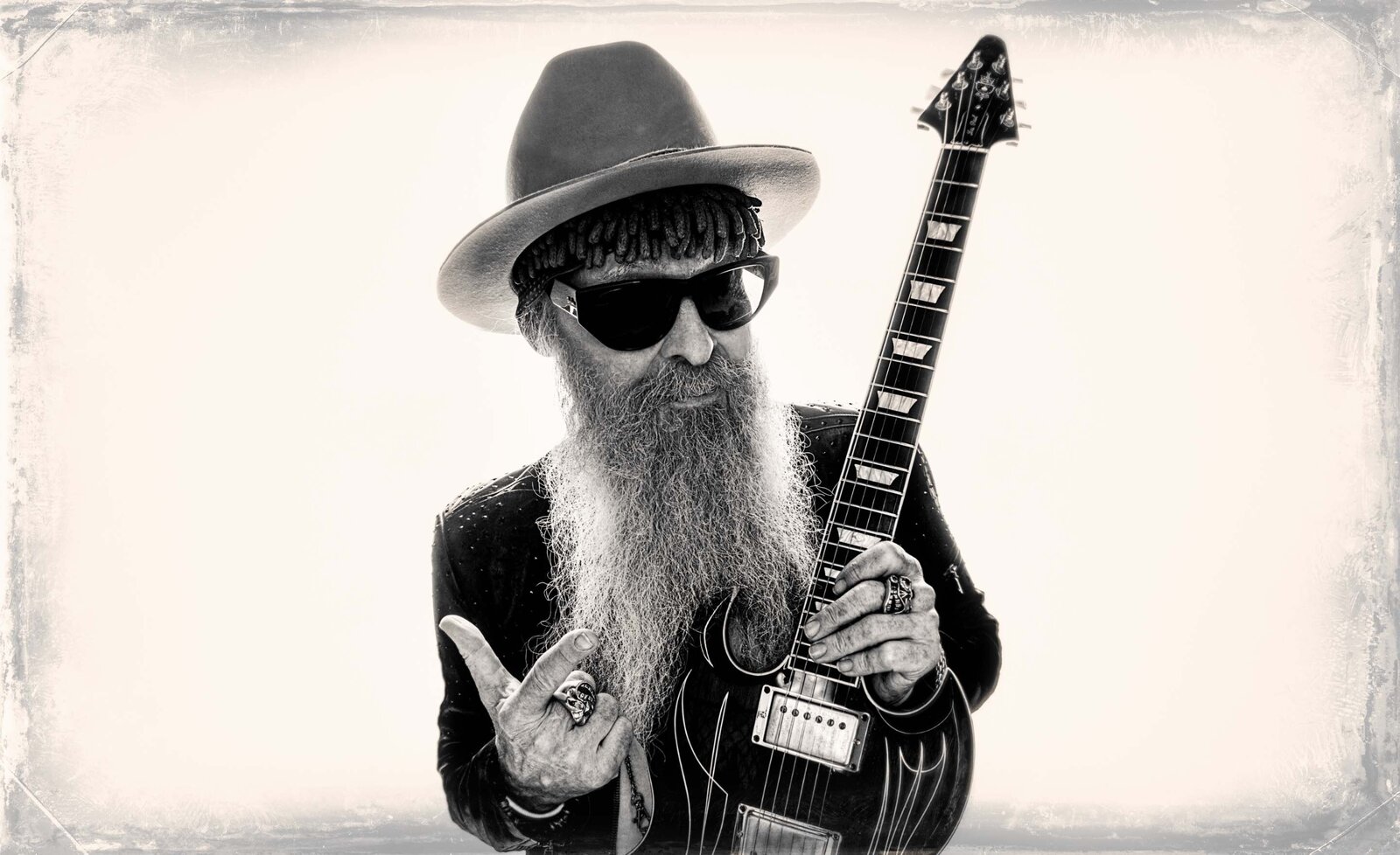 Music portrait Billy Gibbons black and white  holding  guitar pointing  upwards wearing white cowboy hat sunglasses