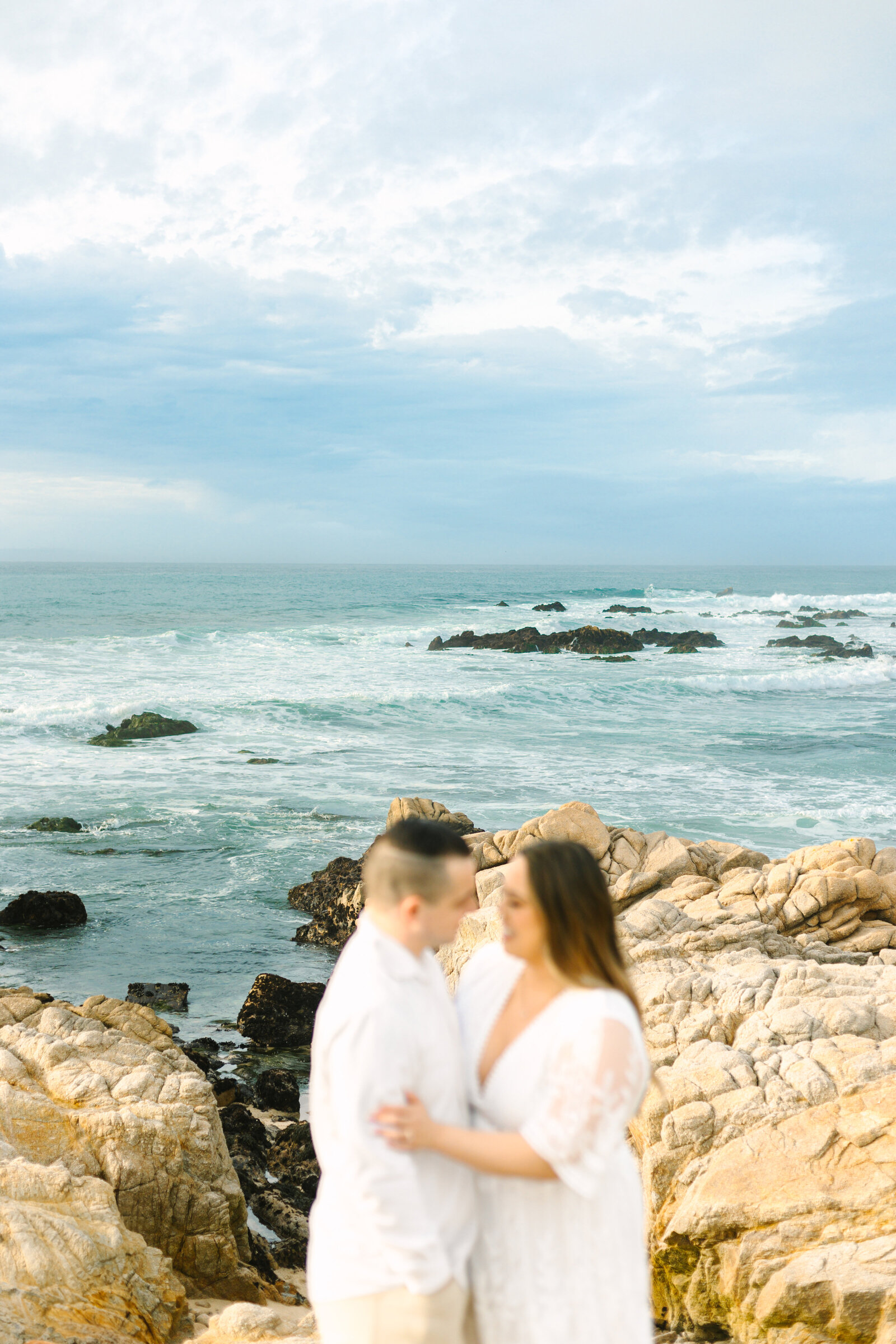 An engaged man and woman take photos on the beach in Pacific Grove, Monterey, California near Big Sur.