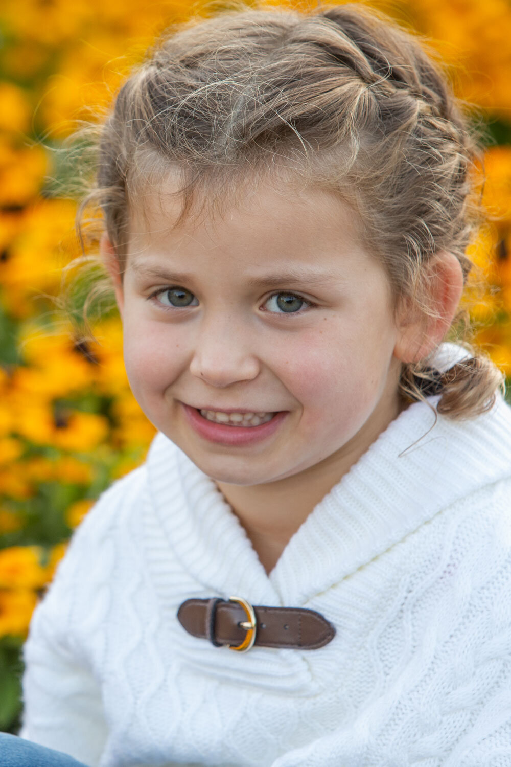 A little girl wearing a white sweater smiles for the camera
