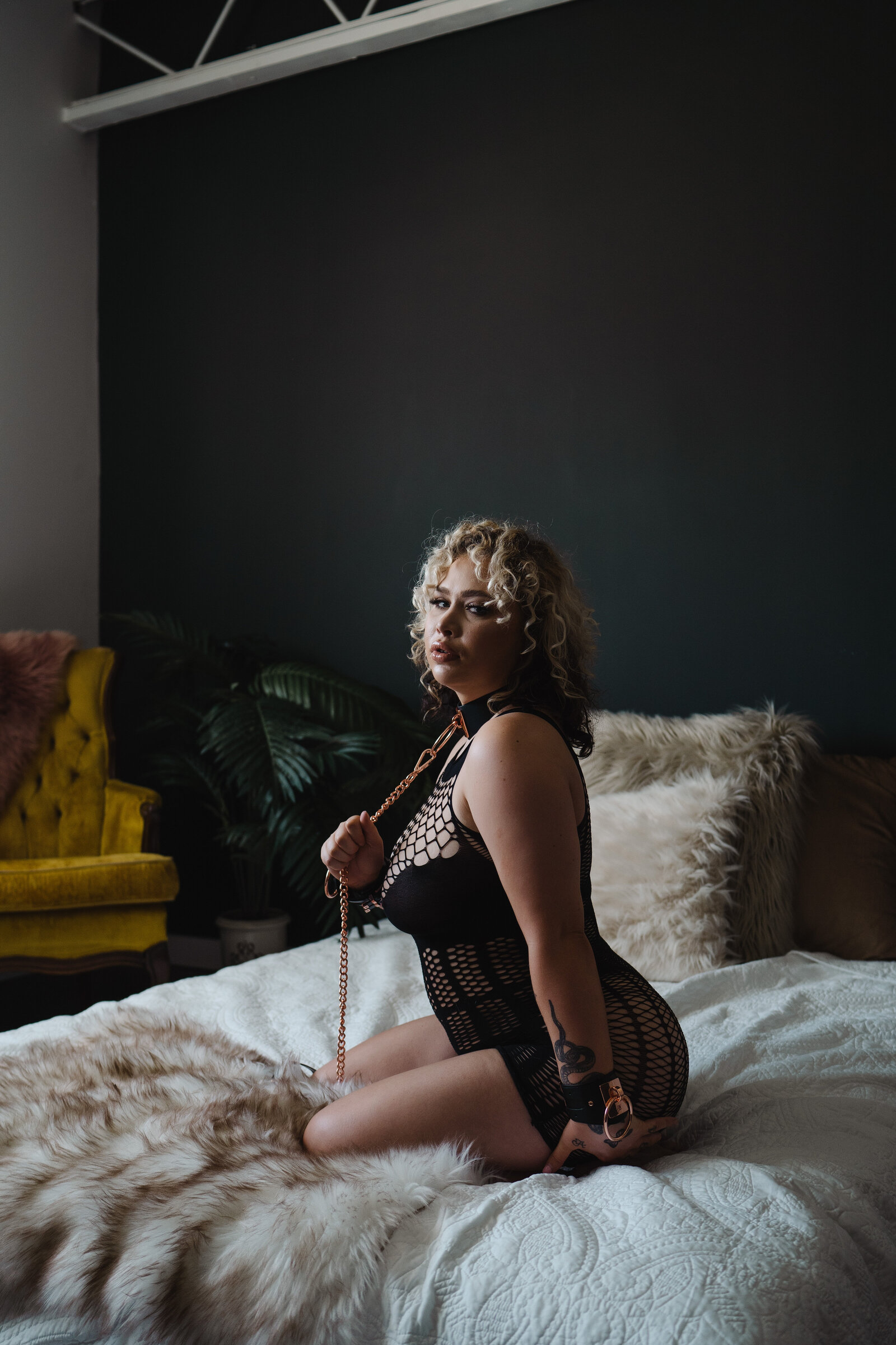 Woman sitting on bed with collar and cuffs on during her boudoir session.