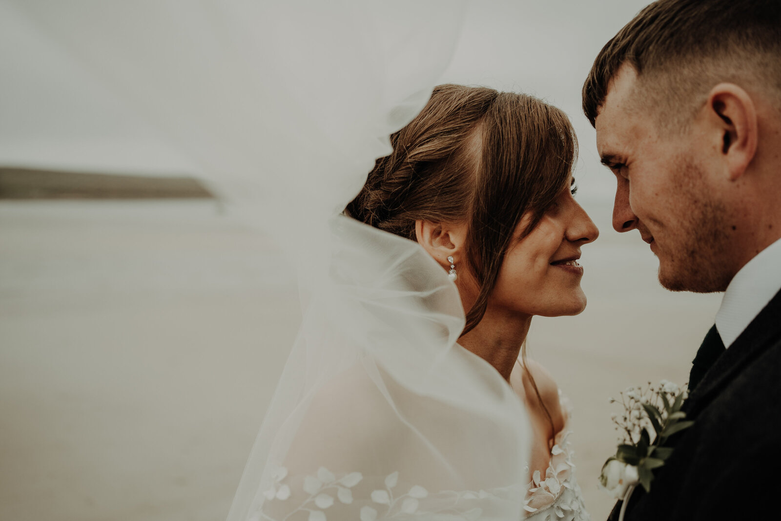 bride with white veil and groom in suit jacket facing each other looking lovingly into each others eyes with the sea in background natural aberdeen wedding photography