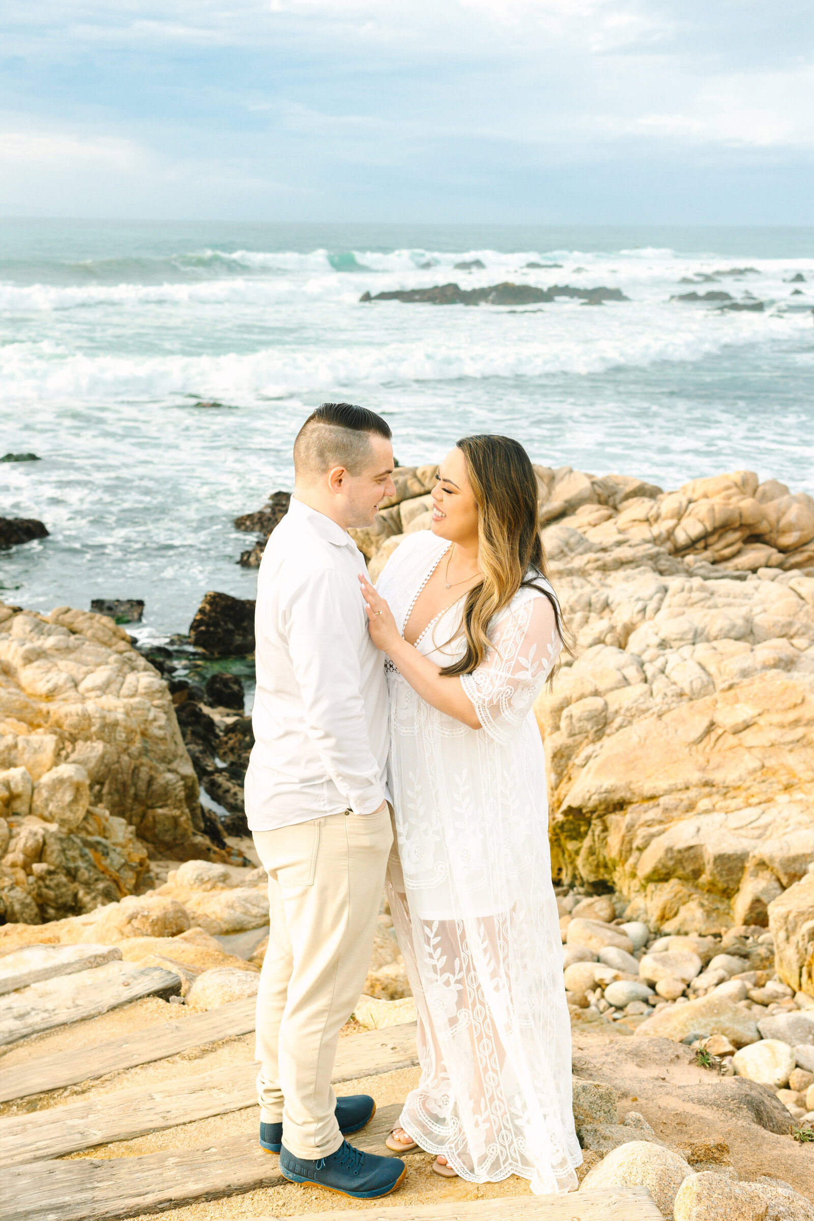 An engaged man and woman take photos on the beach in Pacific Grove, Monterey, California near Big Sur.