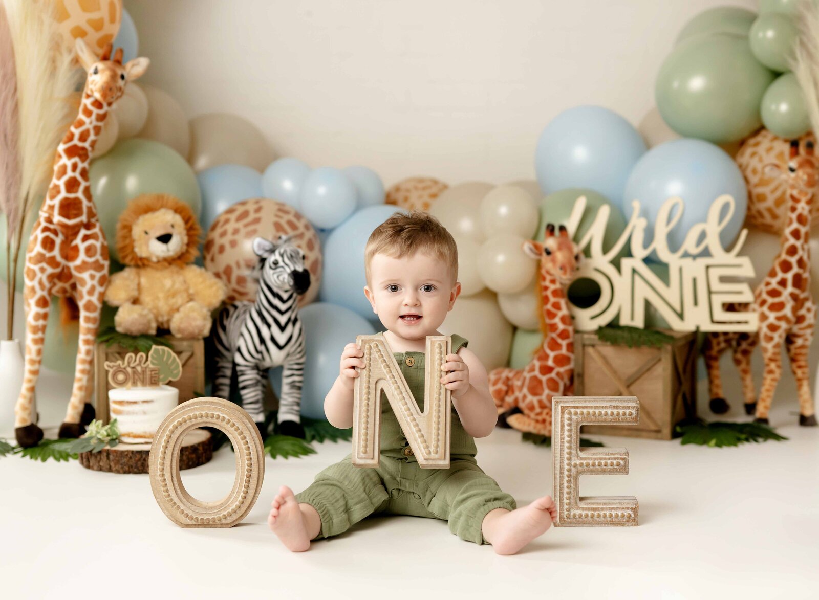 Boy holding ONE letters in front of boho safari themed birthday set.
