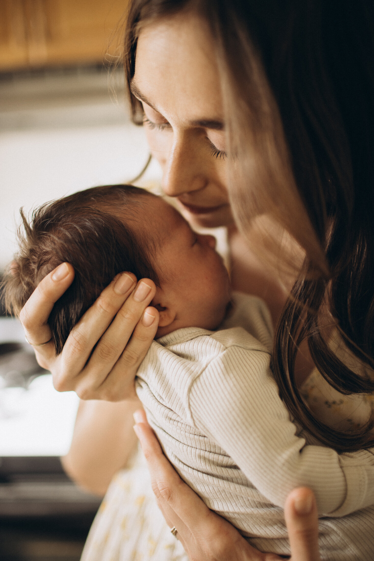 A tender moment as a mother gently holds her newborn baby, softly cradling the infant's head while looking at them with adoration and love. the setting has warm natural lighting.