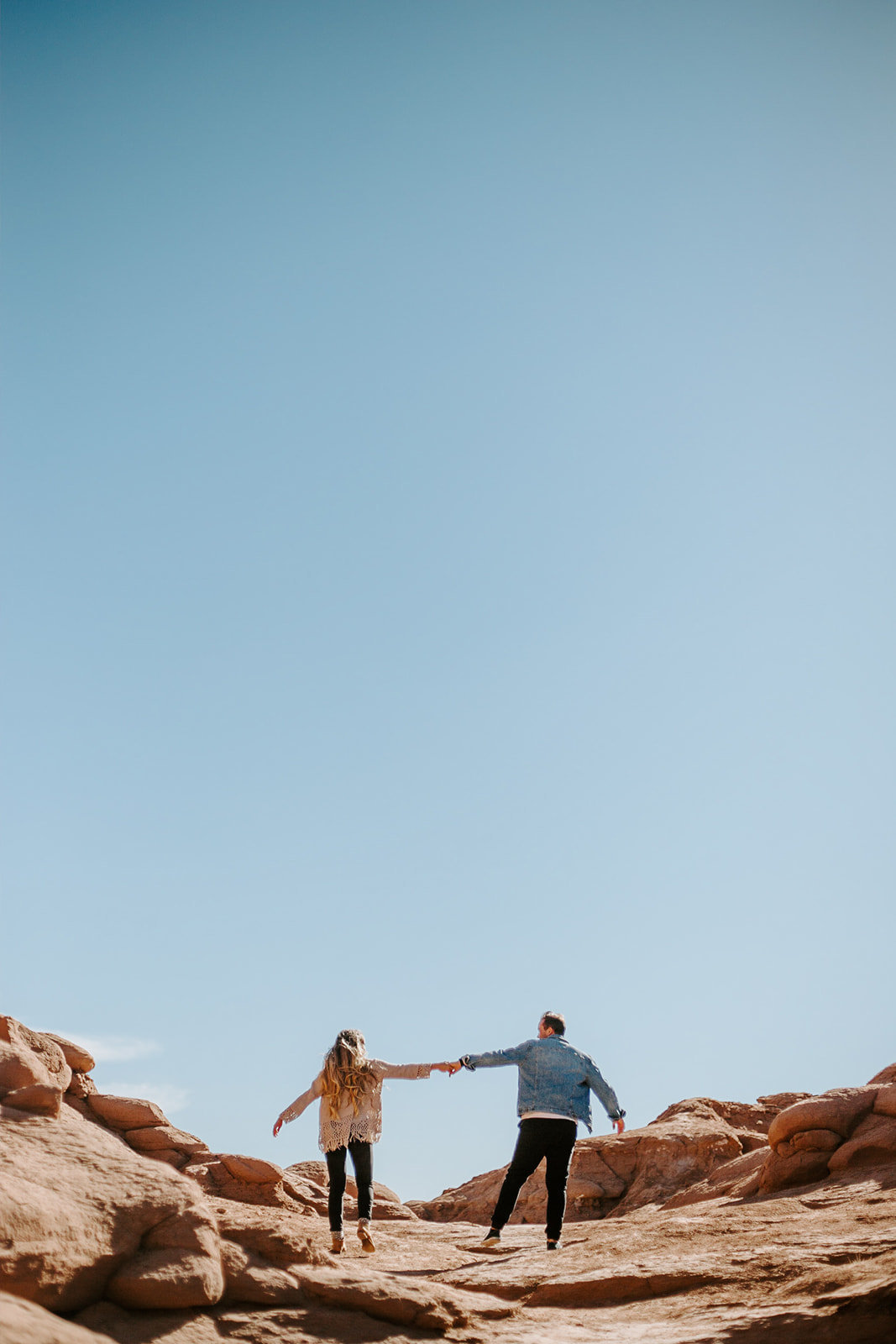 Couple holding hands walking through the arizona rocks during this engagement seession