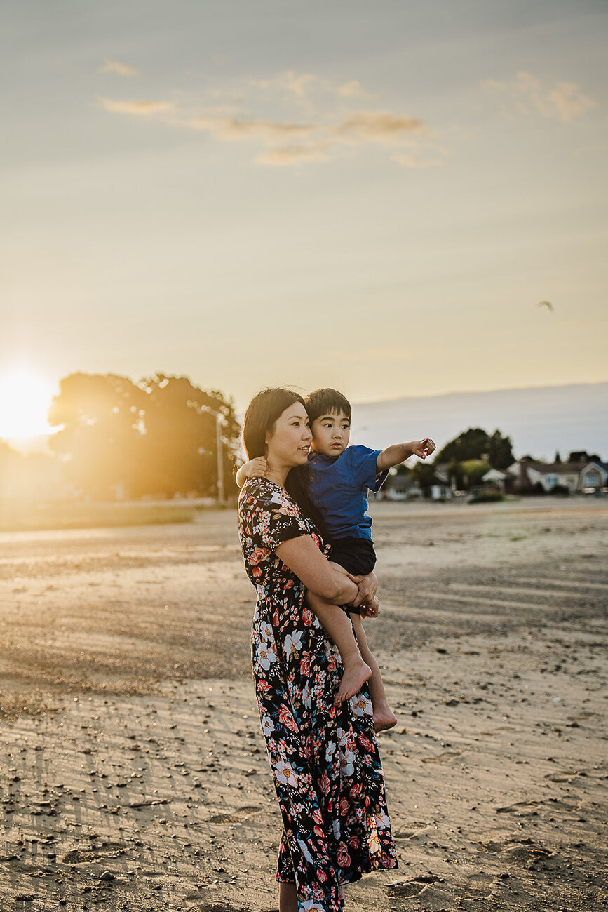 mother holds son on a boston beach at sunset