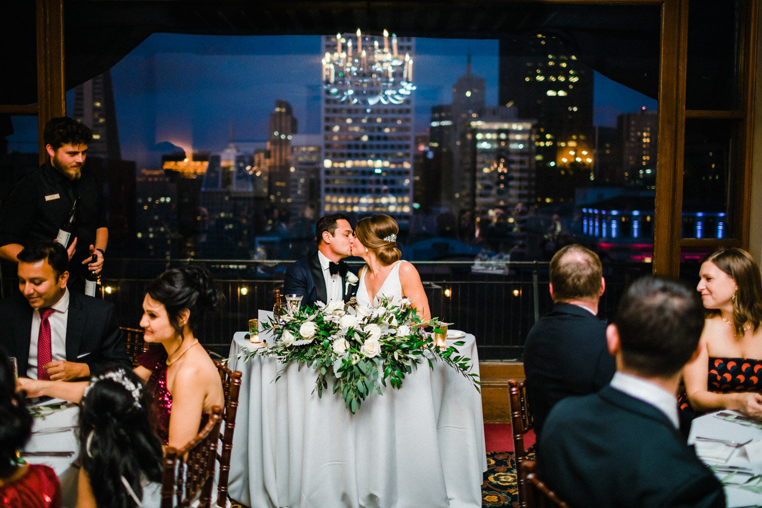 Newlyweds kissing at reception with city skyline view