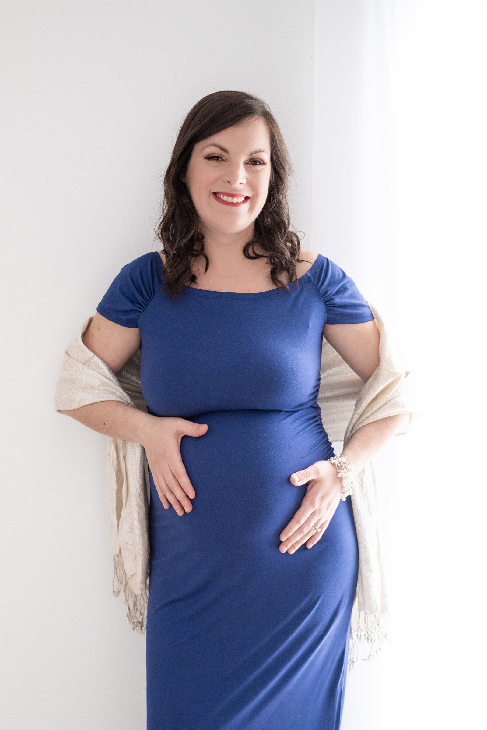 A pregnant woman leaning on  a wall  with her hands on either side of her stomach as she poses for her maternity photos
