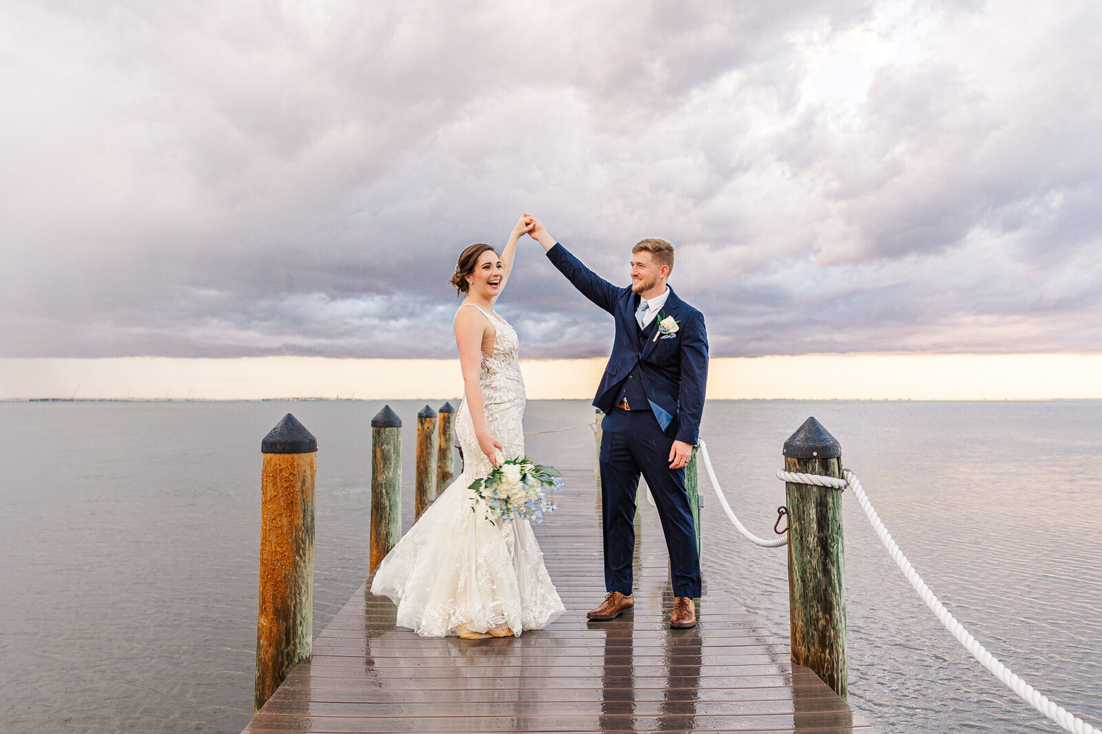 a bride and groom dance on a pier at sunset